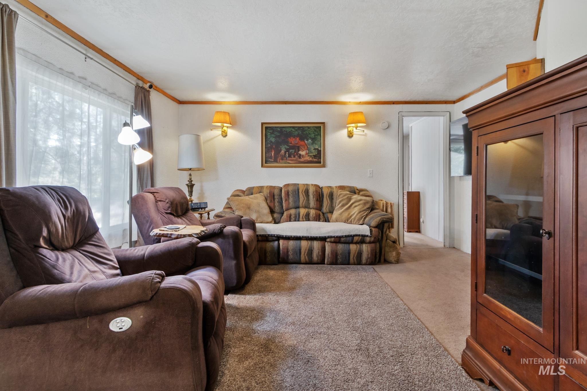 Living area featuring a large window with sheers, wall-mounted sconces, wood trim, and a built-in wood-finish media cabinet with glass doors