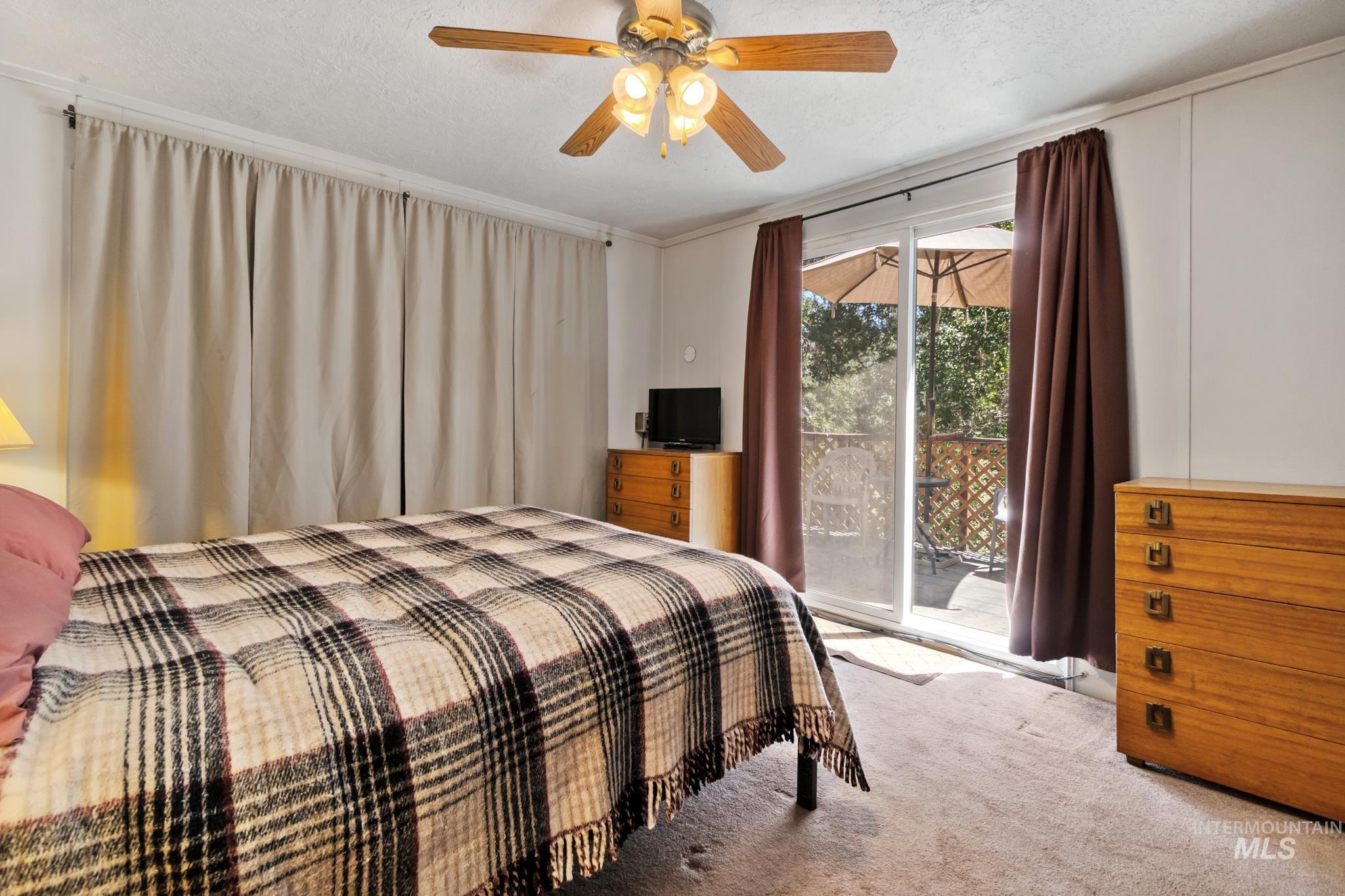 Room featuring sliding glass door access to an exterior deck, a ceiling fan with light fixture, and textured carpeting