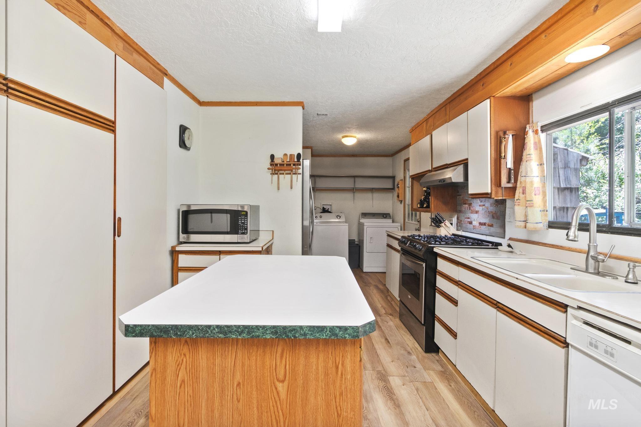 Kitchen featuring a central island with a solid surface countertop, wood-finish flooring, white cabinetry, a built-in stainless steel microwave, and a gas range