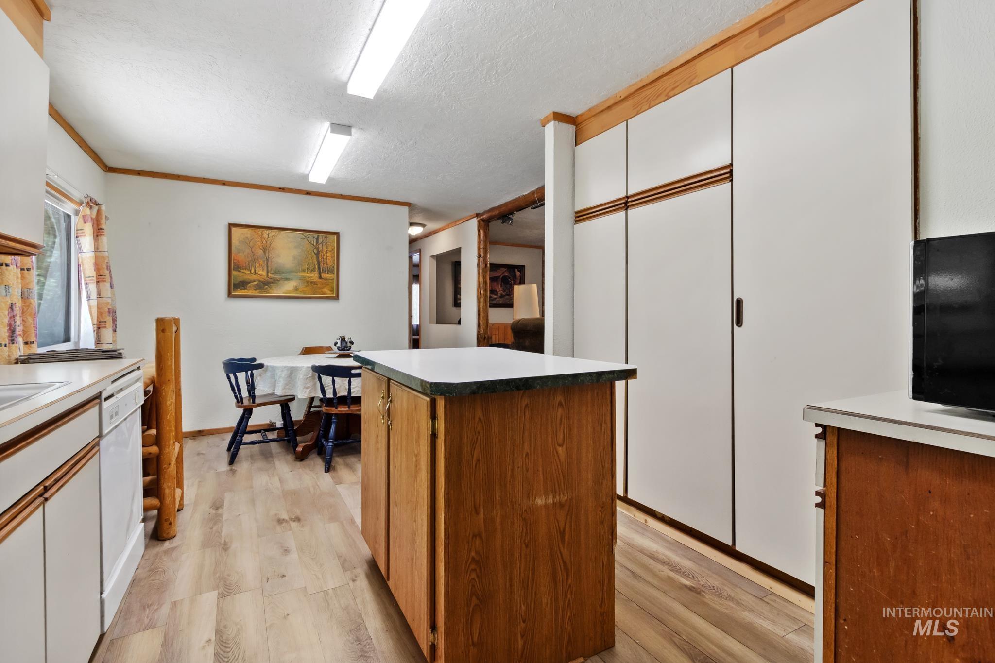 Kitchen area featuring wood-finish flooring, an island with countertop, and white cabinetry