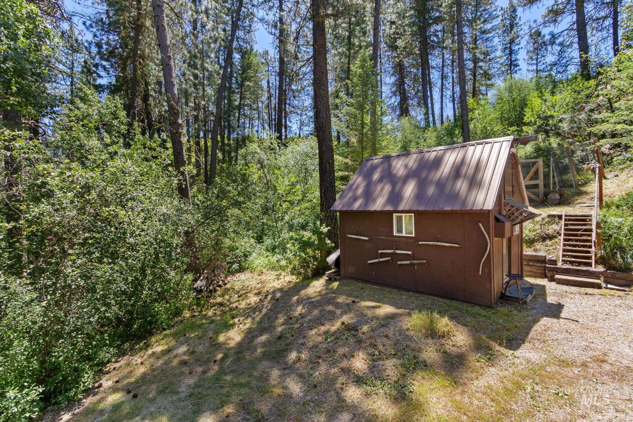 Brown-sided outbuilding with a metal roof, featuring a single window and rustic branch detailing