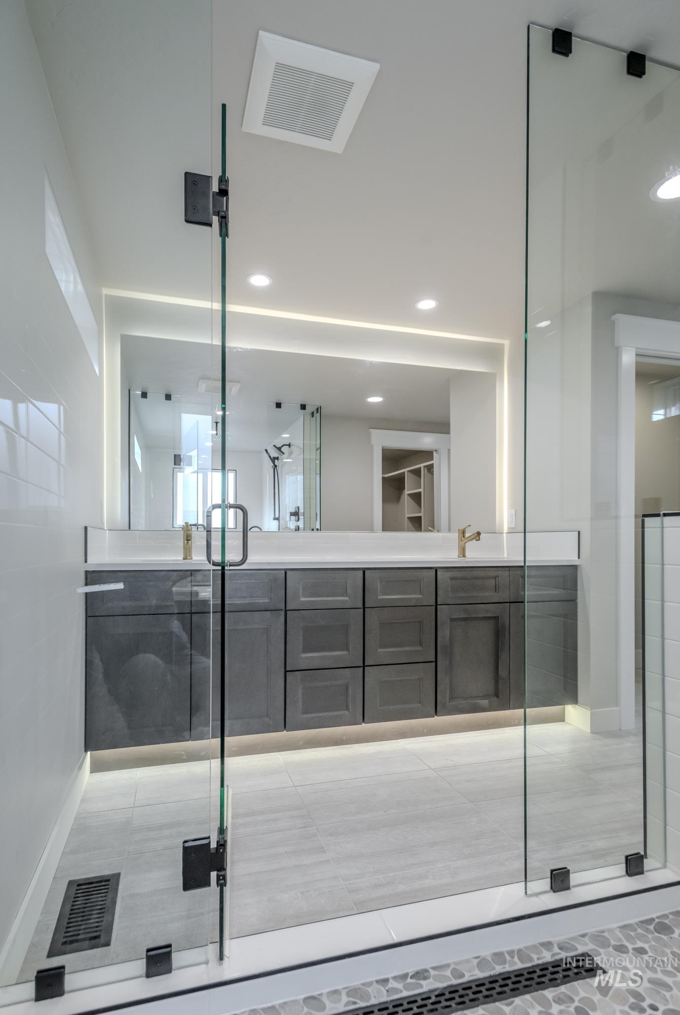 Full bathroom featuring double vanity, a wet-room, recessed lighting, backlit mirror, and lighted base boards.