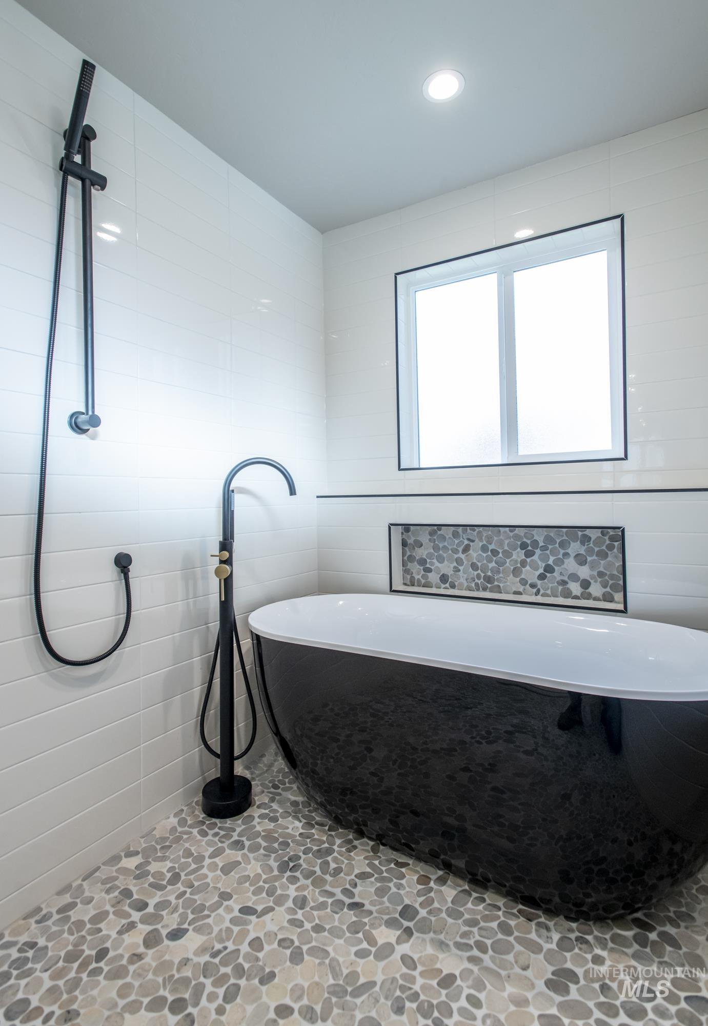 Soaker tub bath featuring a freestanding bath, freestanding filler, hand wand, recessed lighting, and tile walls.