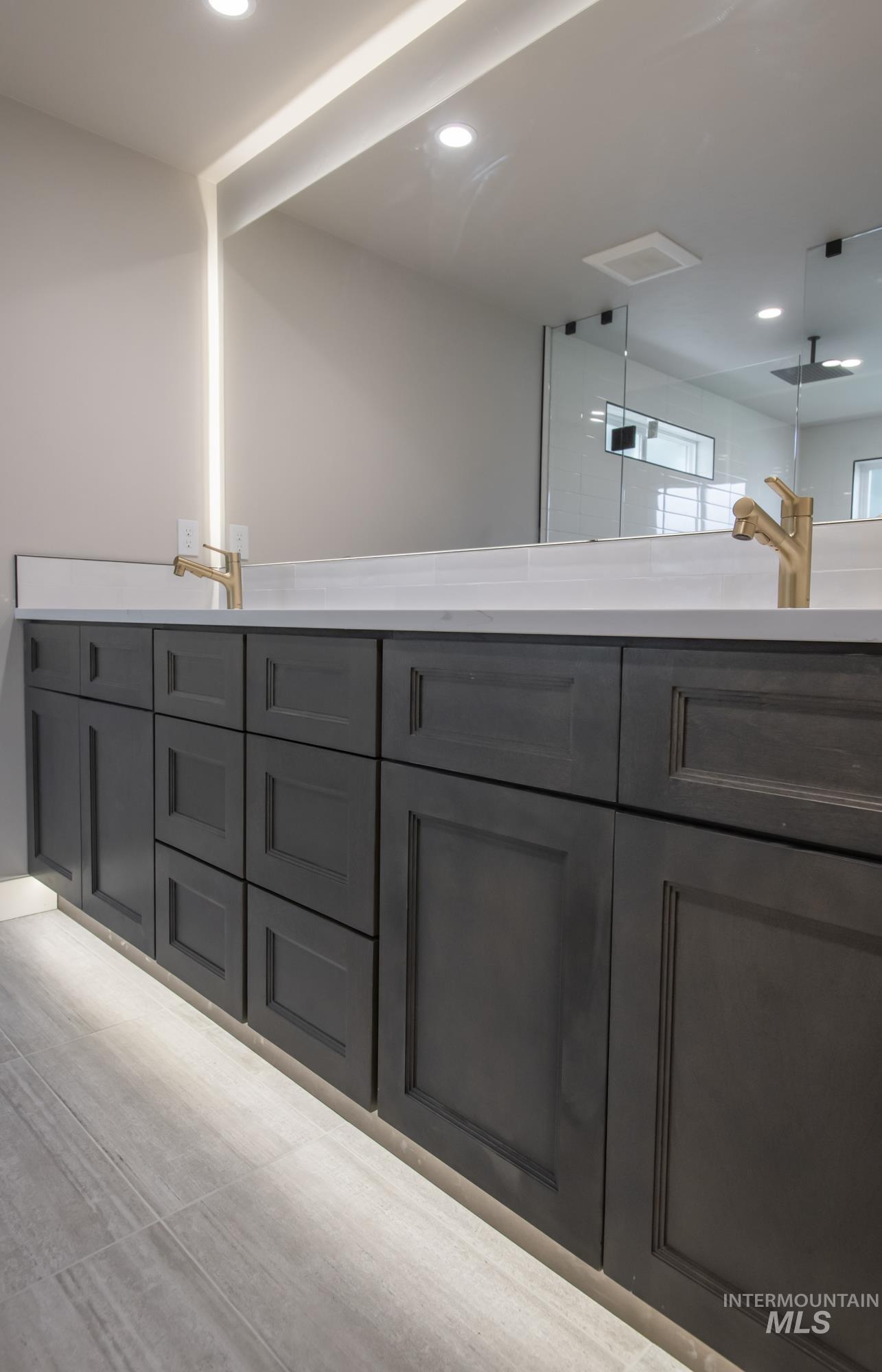 Primary Bathroom view of wet-room reflected in the massive backlit mirror and dual vanity with kickboard lighting.