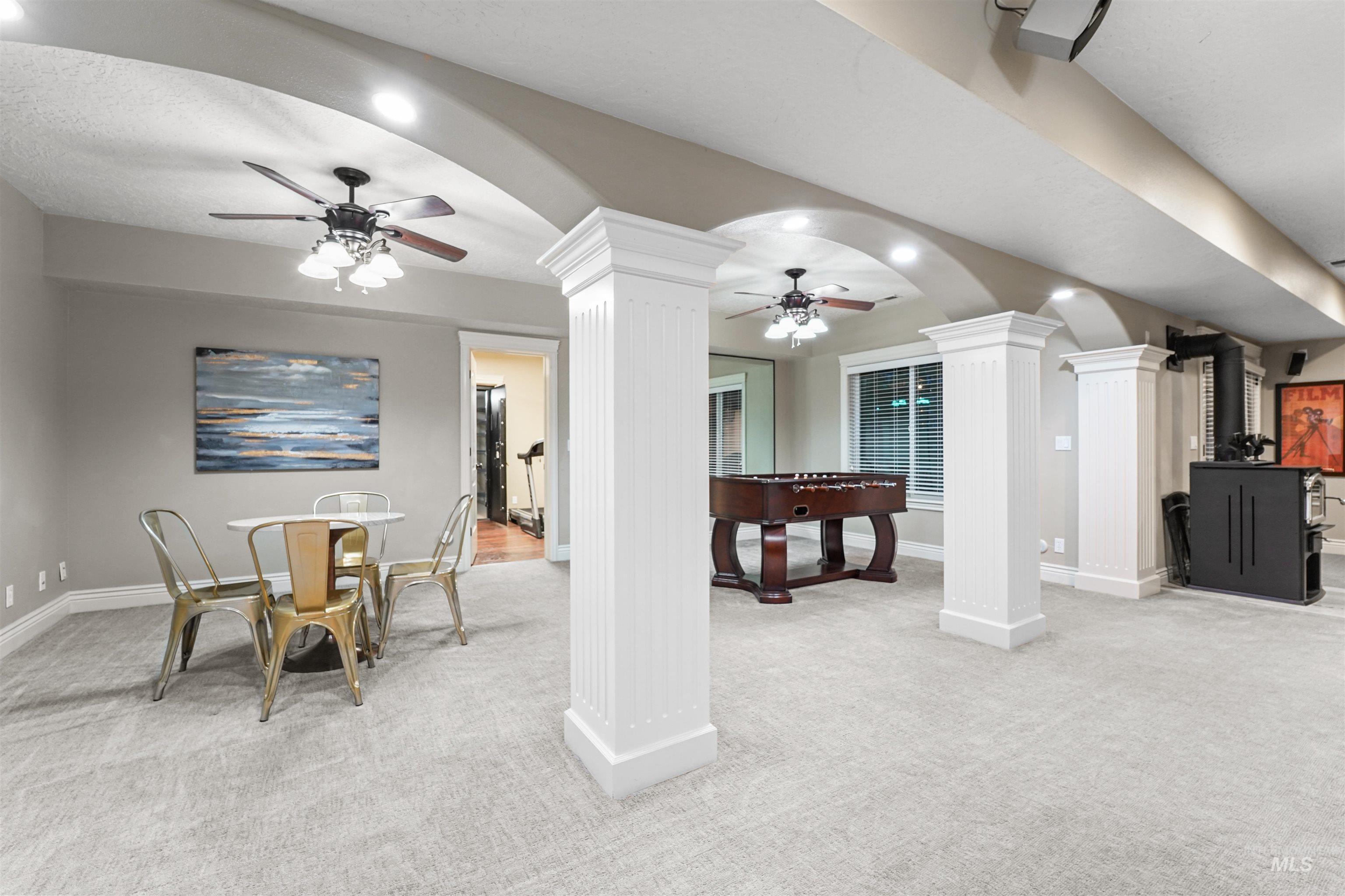 Rec room with decorative columns, light carpet, ceiling fan, and arched walkways
