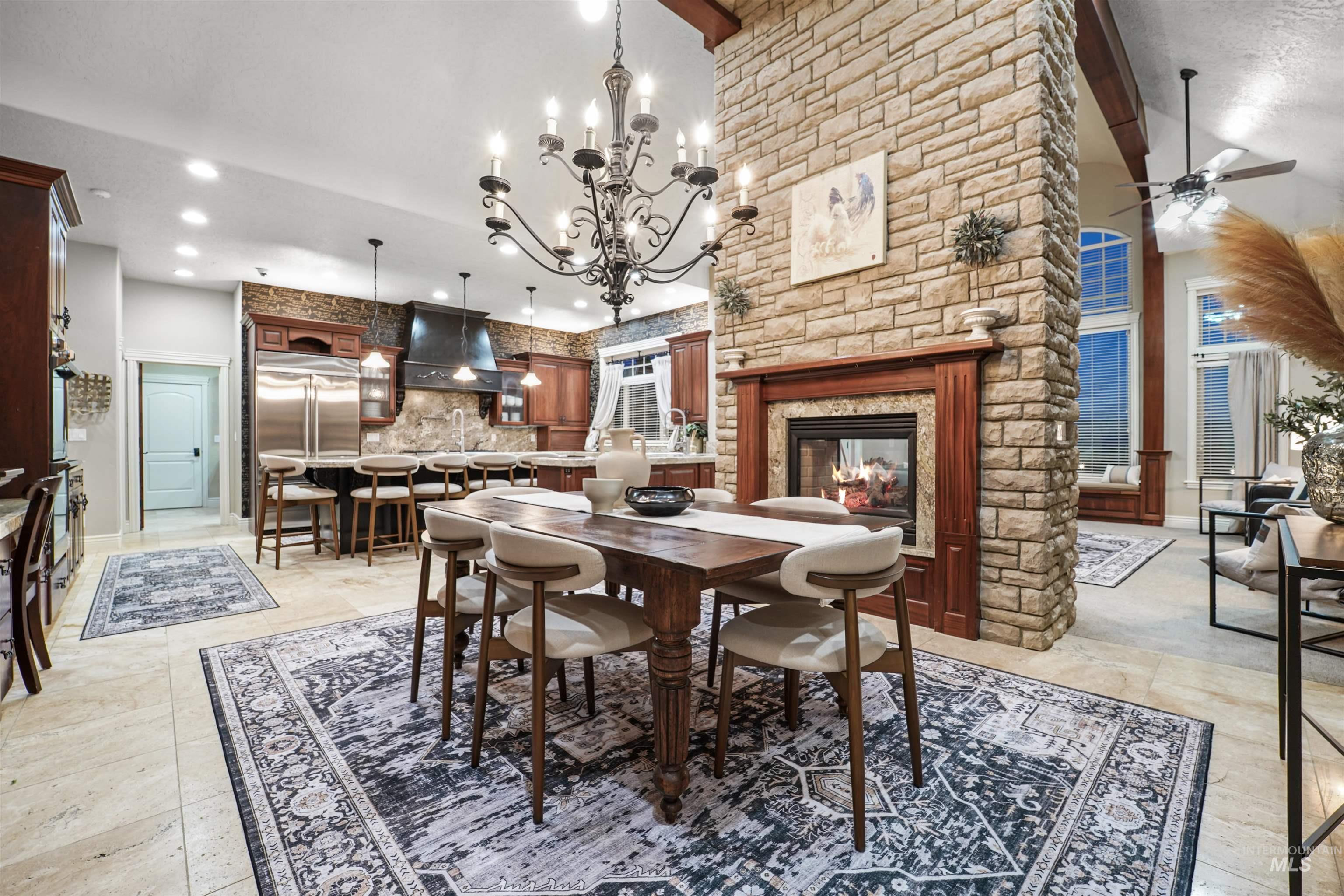 Dining area featuring high vaulted ceiling, a stone fireplace, ceiling fan, a chandelier, and recessed lighting