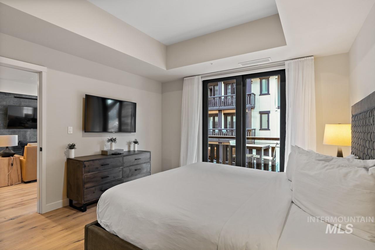 Bedroom featuring access to exterior, light wood finished floors, and a raised ceiling