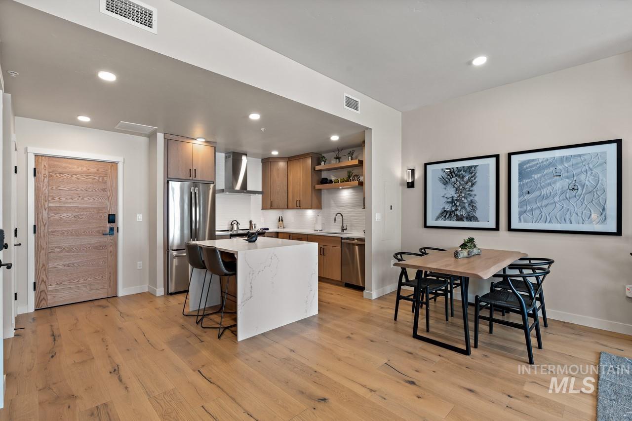 Kitchen featuring wall chimney exhaust hood, appliances with stainless steel finishes, open shelves, light wood-type flooring, and recessed lighting
