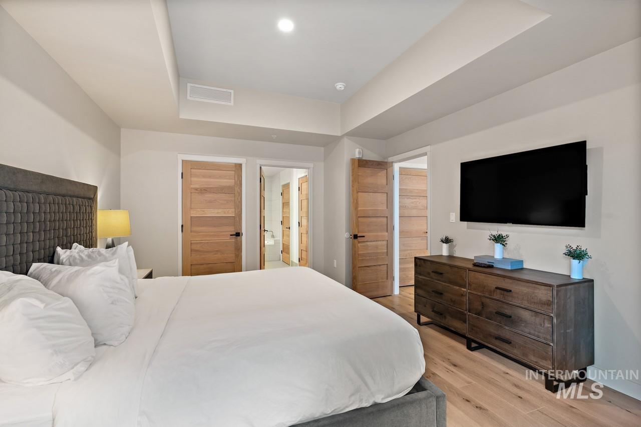 Bedroom featuring light wood finished floors, a tray ceiling, and connected bathroom