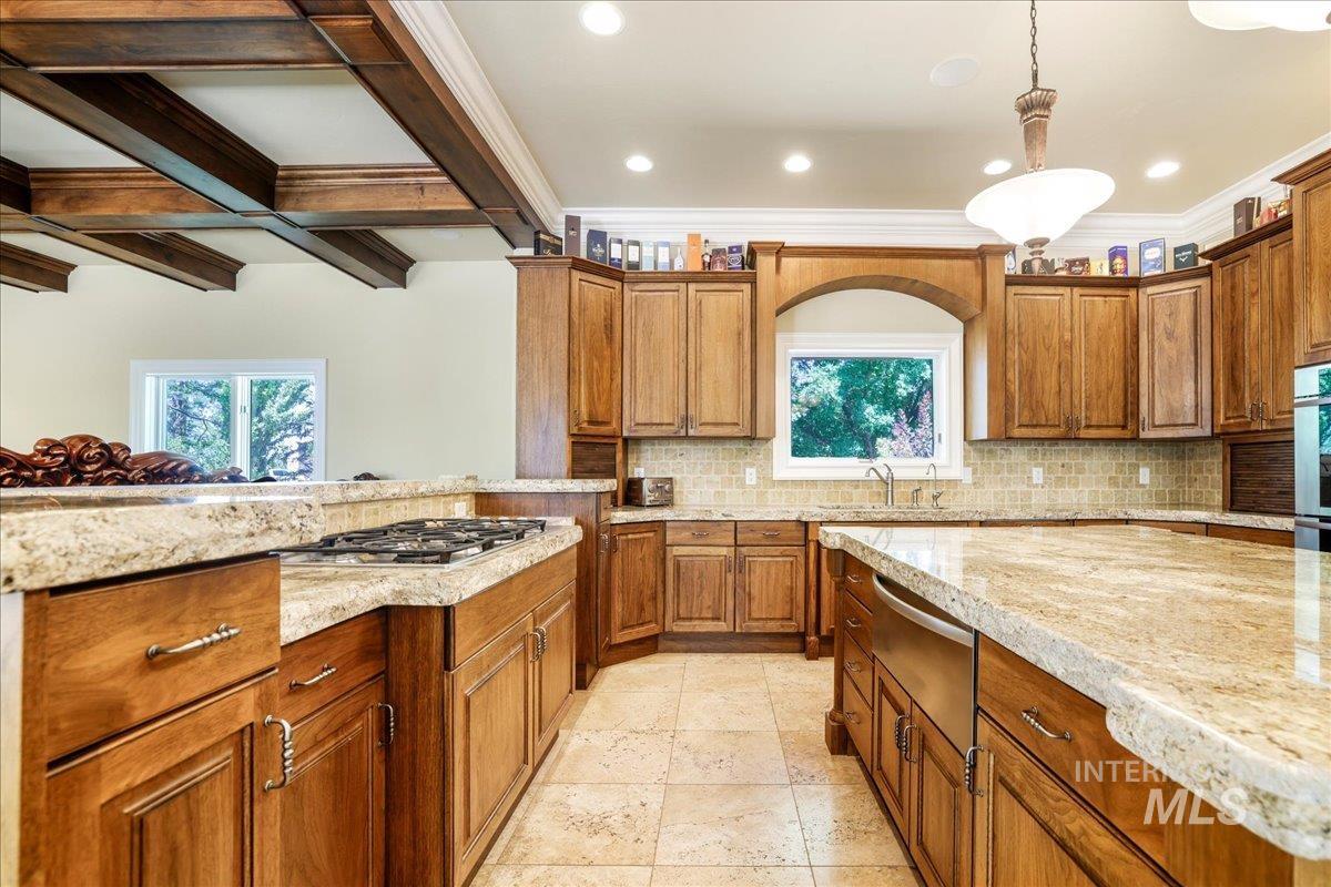 Kitchen with brown cabinets, light stone counters, tasteful backsplash, a warming drawer, and decorative light fixtures