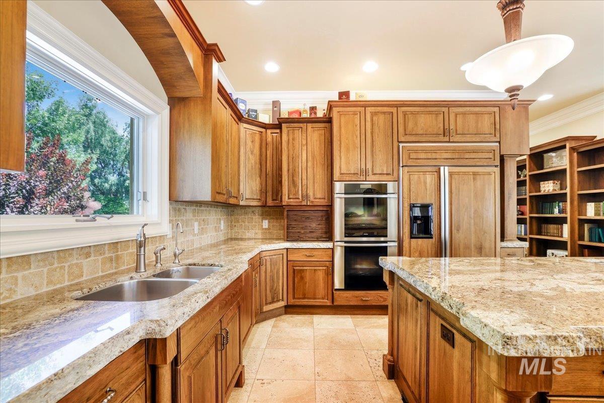 Kitchen featuring double oven, brown cabinetry, tasteful backsplash, light stone counters, and ornamental molding