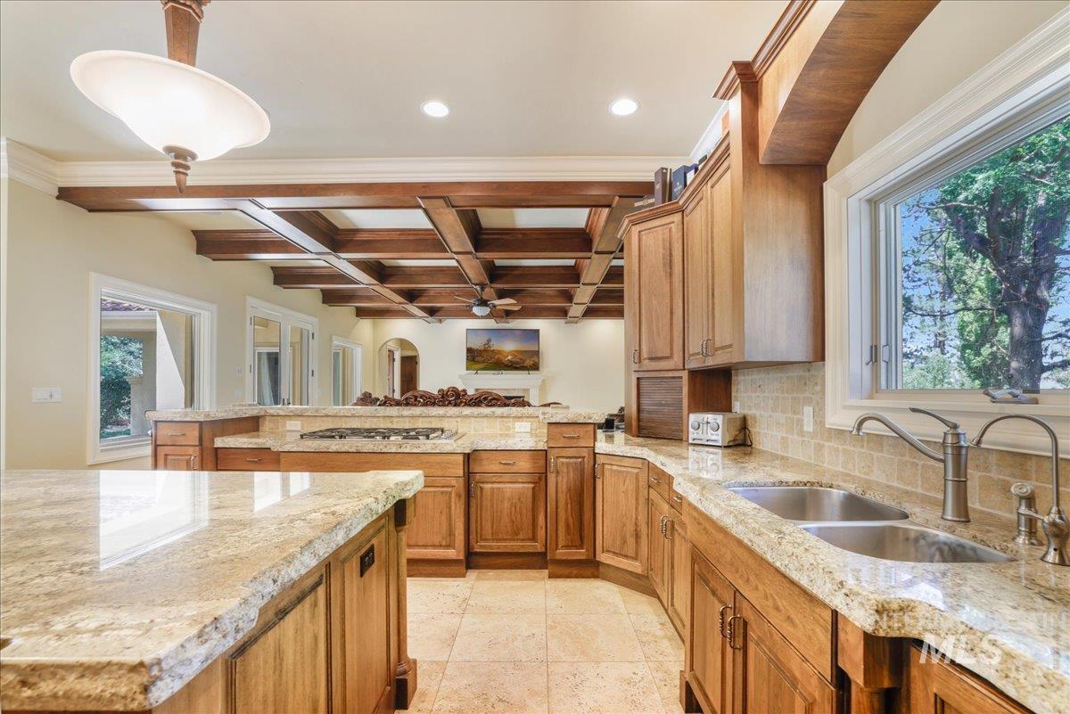 Kitchen with ceiling fan, tasteful backsplash, a peninsula, coffered ceiling, and light stone countertops
