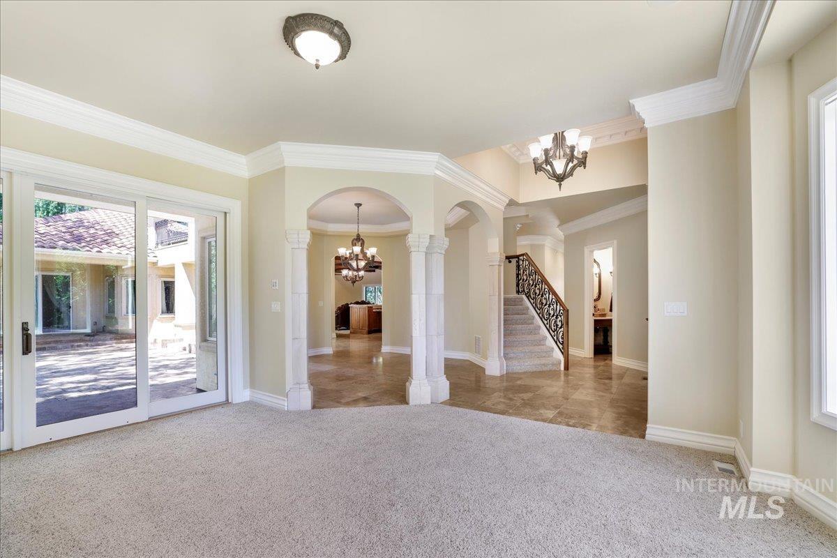 Unfurnished room featuring a chandelier, arched walkways, stairway, carpet floors, and ornate columns