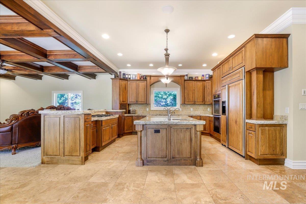 Kitchen with brown cabinets, recessed lighting, an island with sink, open floor plan, and light stone countertops