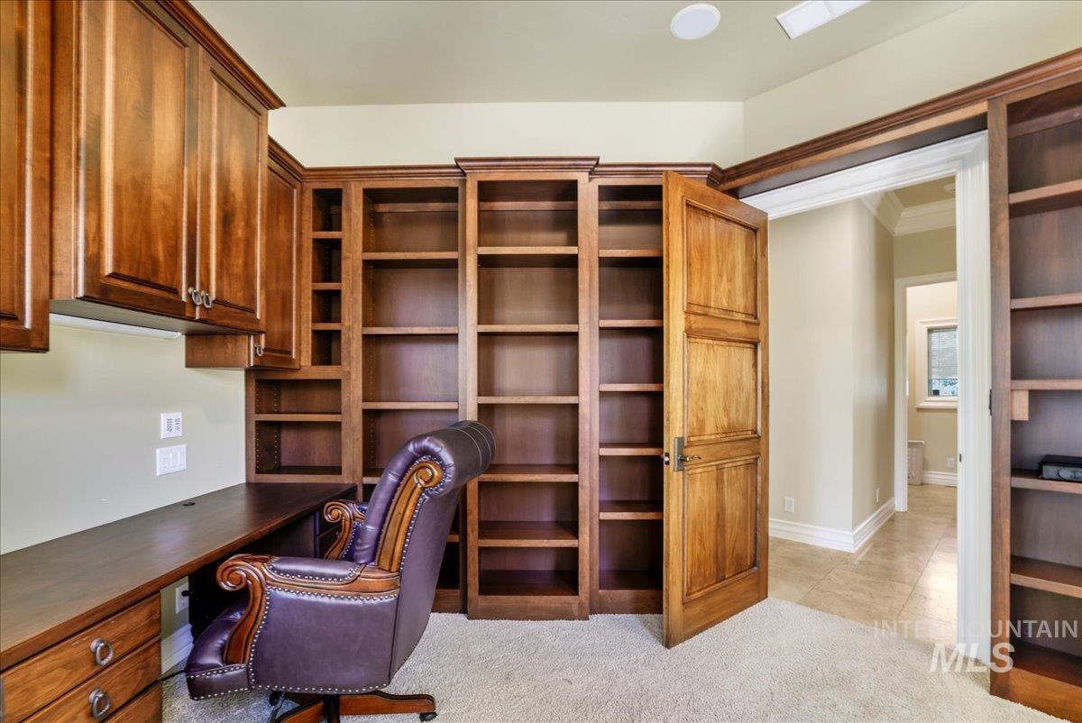 Unfurnished office featuring built in desk, light carpet, crown molding, and light tile patterned flooring