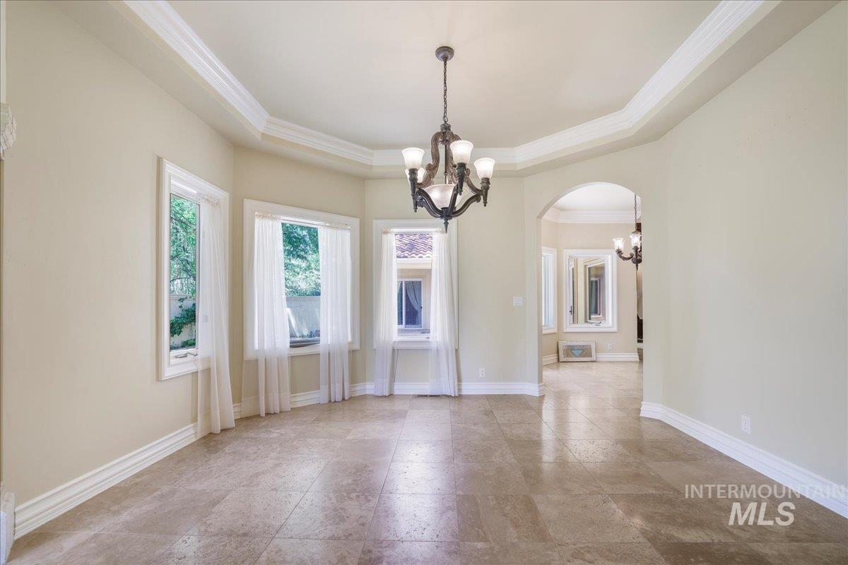 Unfurnished room featuring a chandelier, arched walkways, a tray ceiling, and ornamental molding
