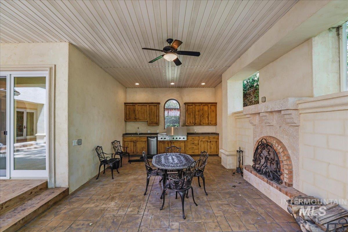 View of patio / terrace featuring an outdoor brick fireplace, an outdoor kitchen, a ceiling fan, and outdoor dining area