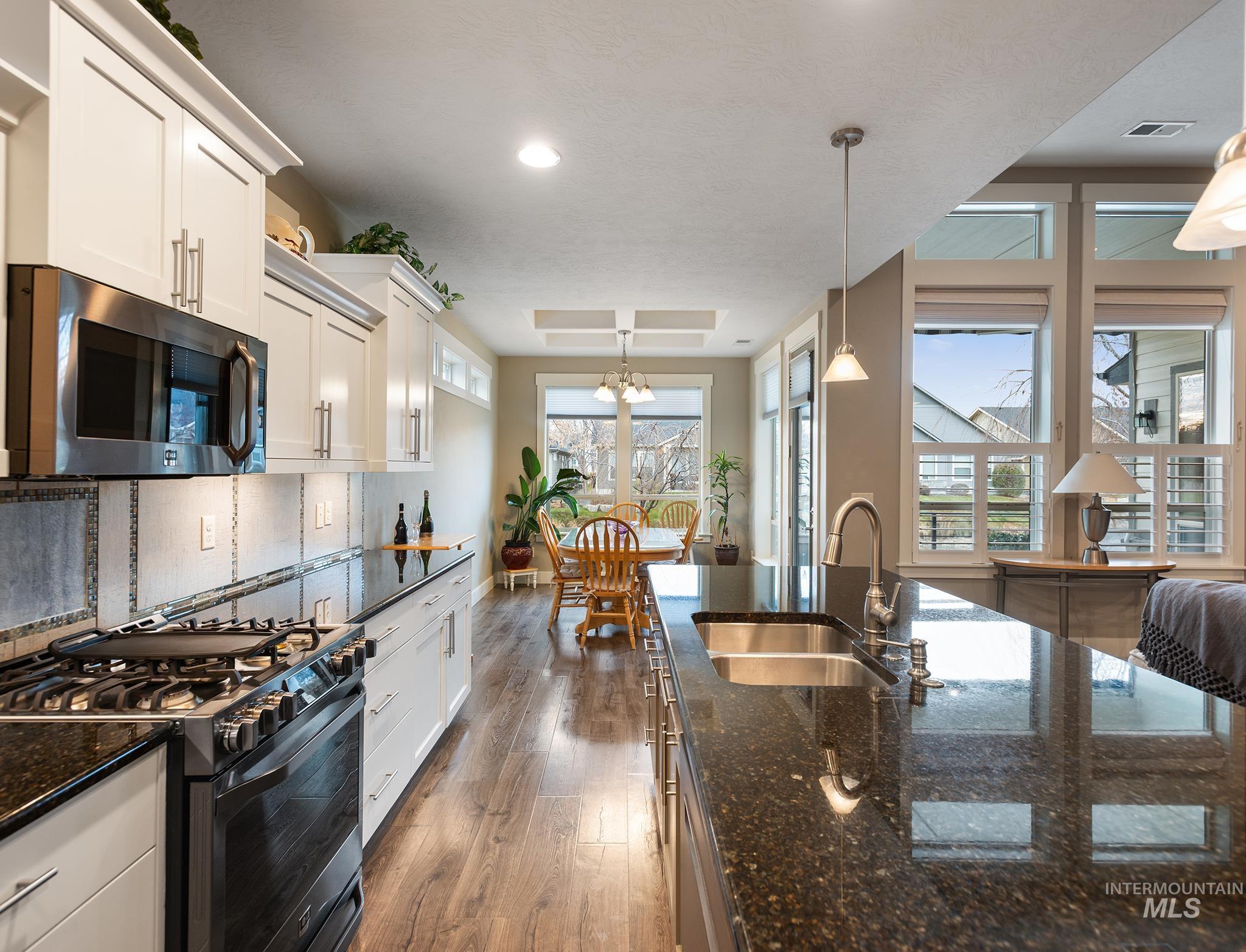 Kitchen featuring appliances with stainless steel finishes, dark stone countertops, pendant lighting, white cabinetry, and dark wood finished floors