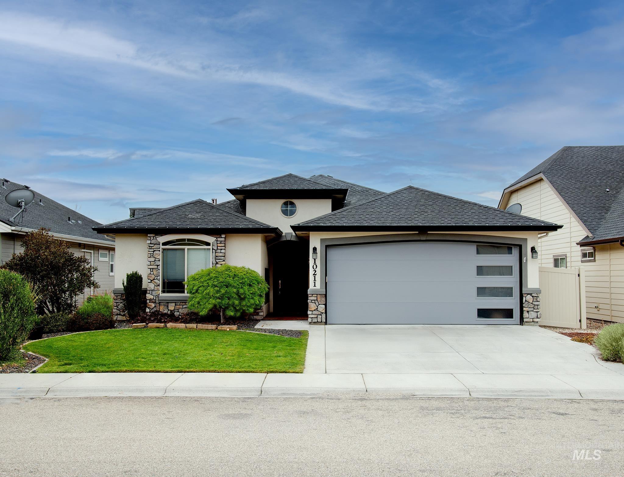 Prairie-style house with stone siding, a front lawn, driveway, an attached garage, and roof with shingles