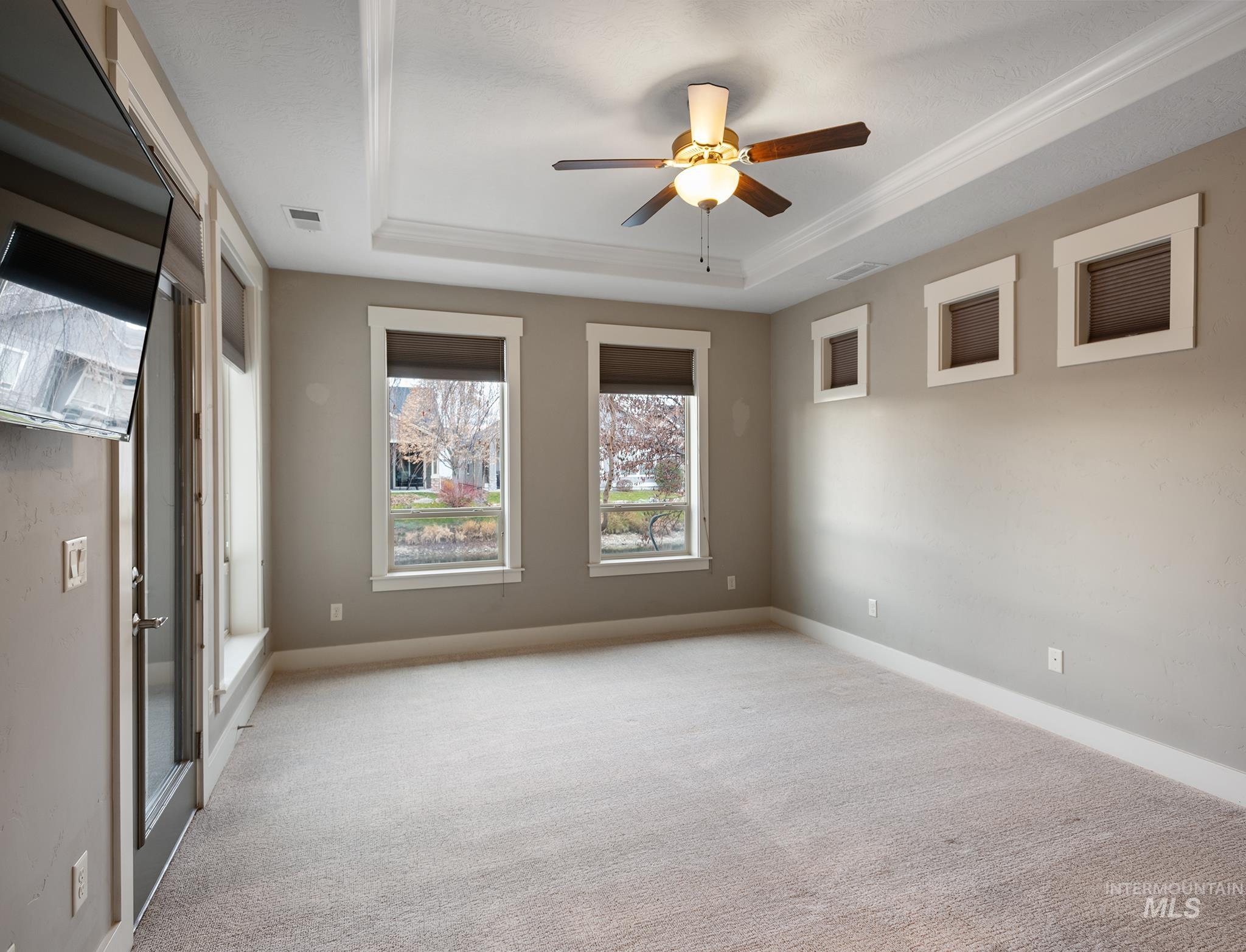Spare room featuring a raised ceiling, light carpet, ceiling fan, and crown molding