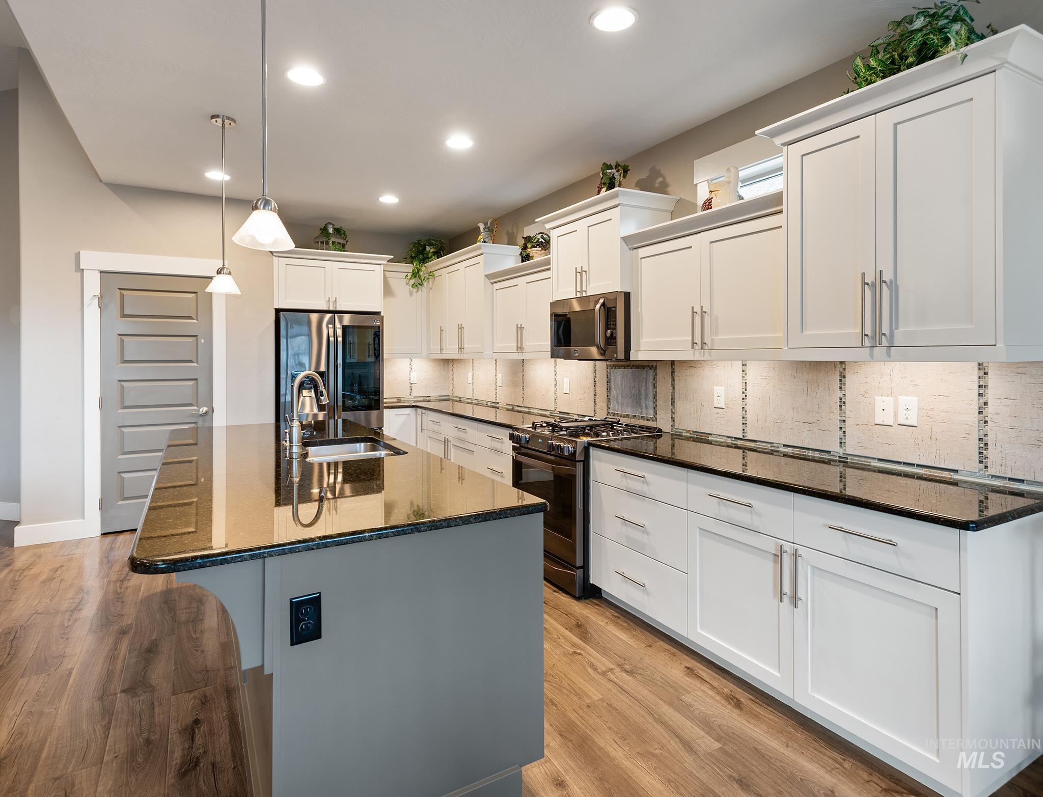 Kitchen featuring backsplash, appliances with stainless steel finishes, dark stone countertops, pendant lighting, and white cabinetry