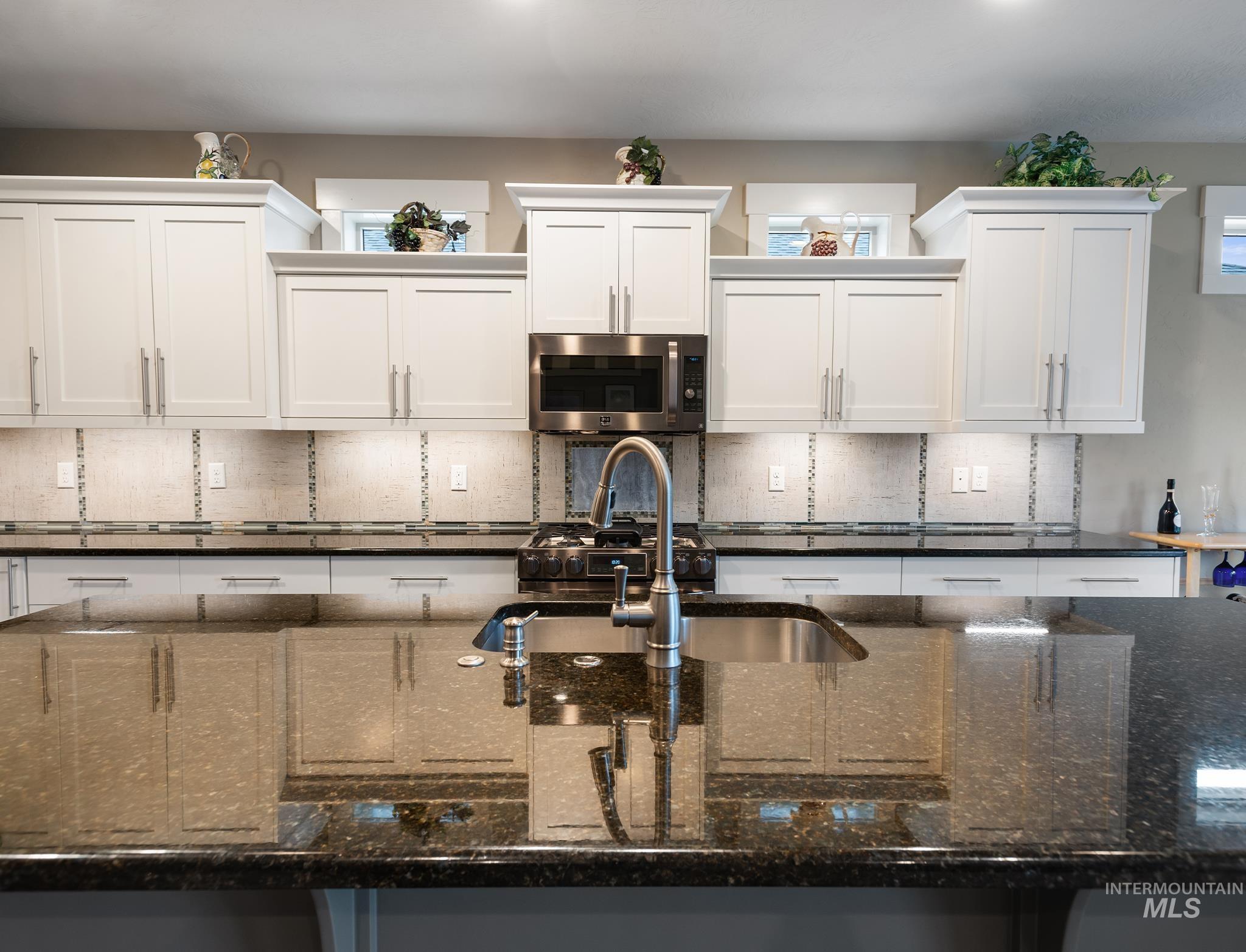 Kitchen with decorative backsplash, dark stone counters, appliances with stainless steel finishes, and white cabinetry