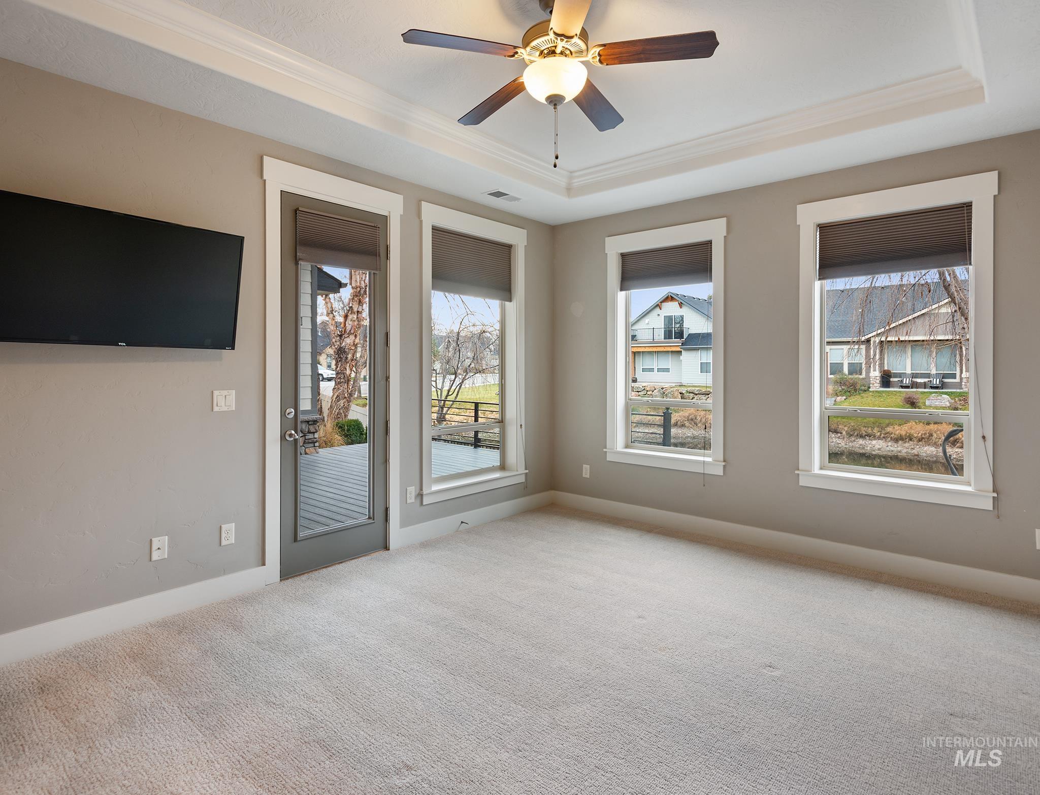 Carpeted empty room with crown molding, a raised ceiling, and a ceiling fan