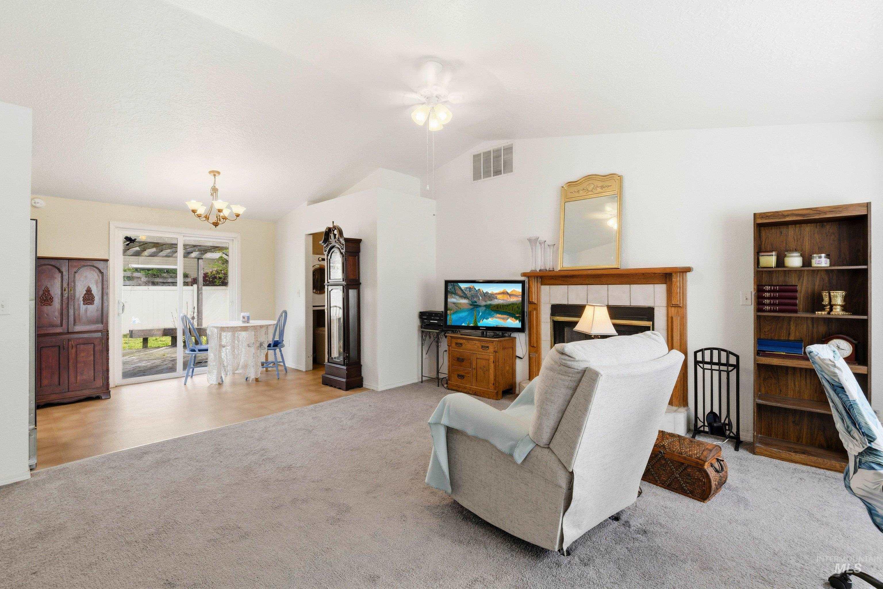 Living area with lofted ceiling, light carpet, a chandelier, ceiling fan, and a tile fireplace