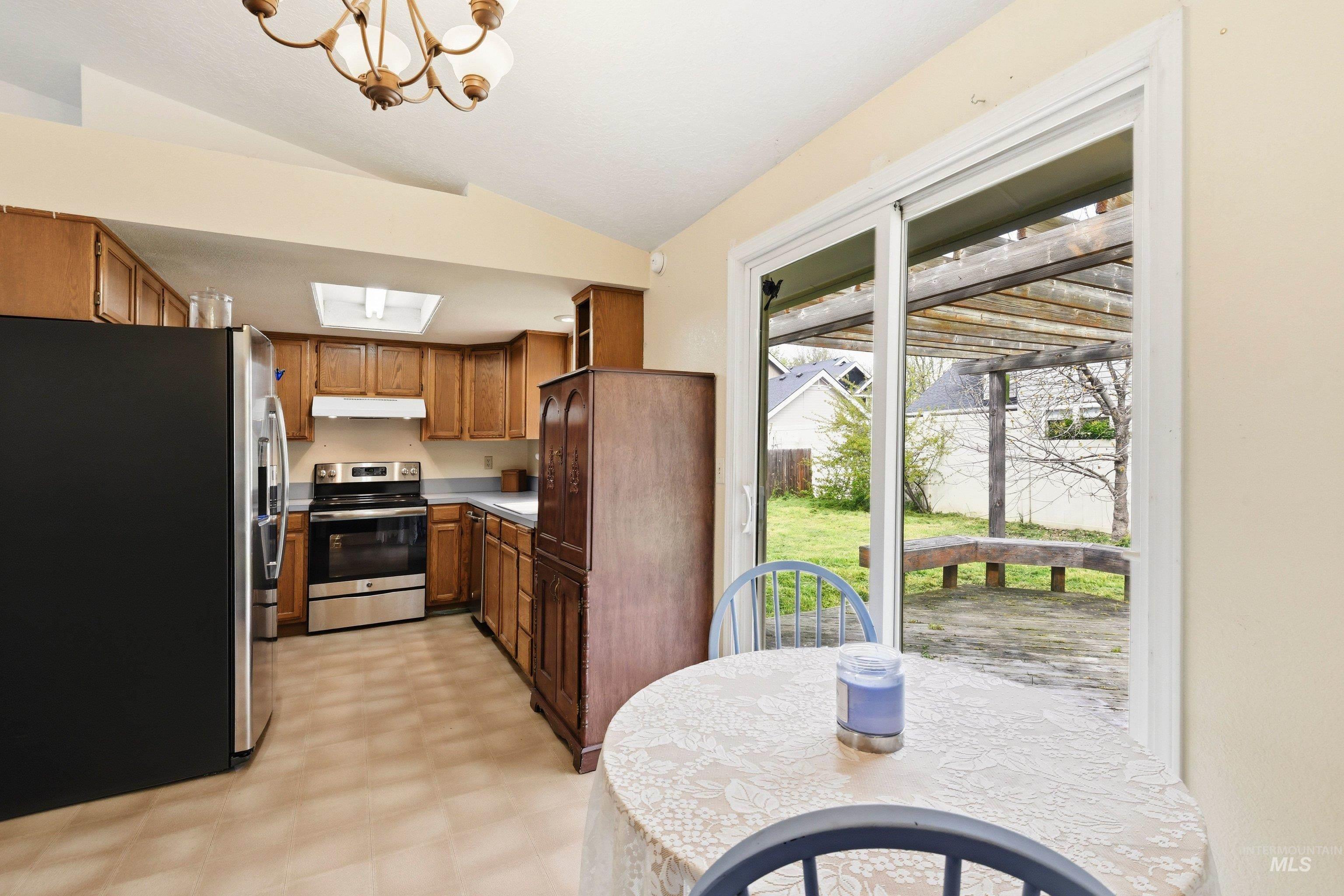 Kitchen featuring stainless steel appliances, light floors, wood finish cabinets, lofted ceiling, and a chandelier
