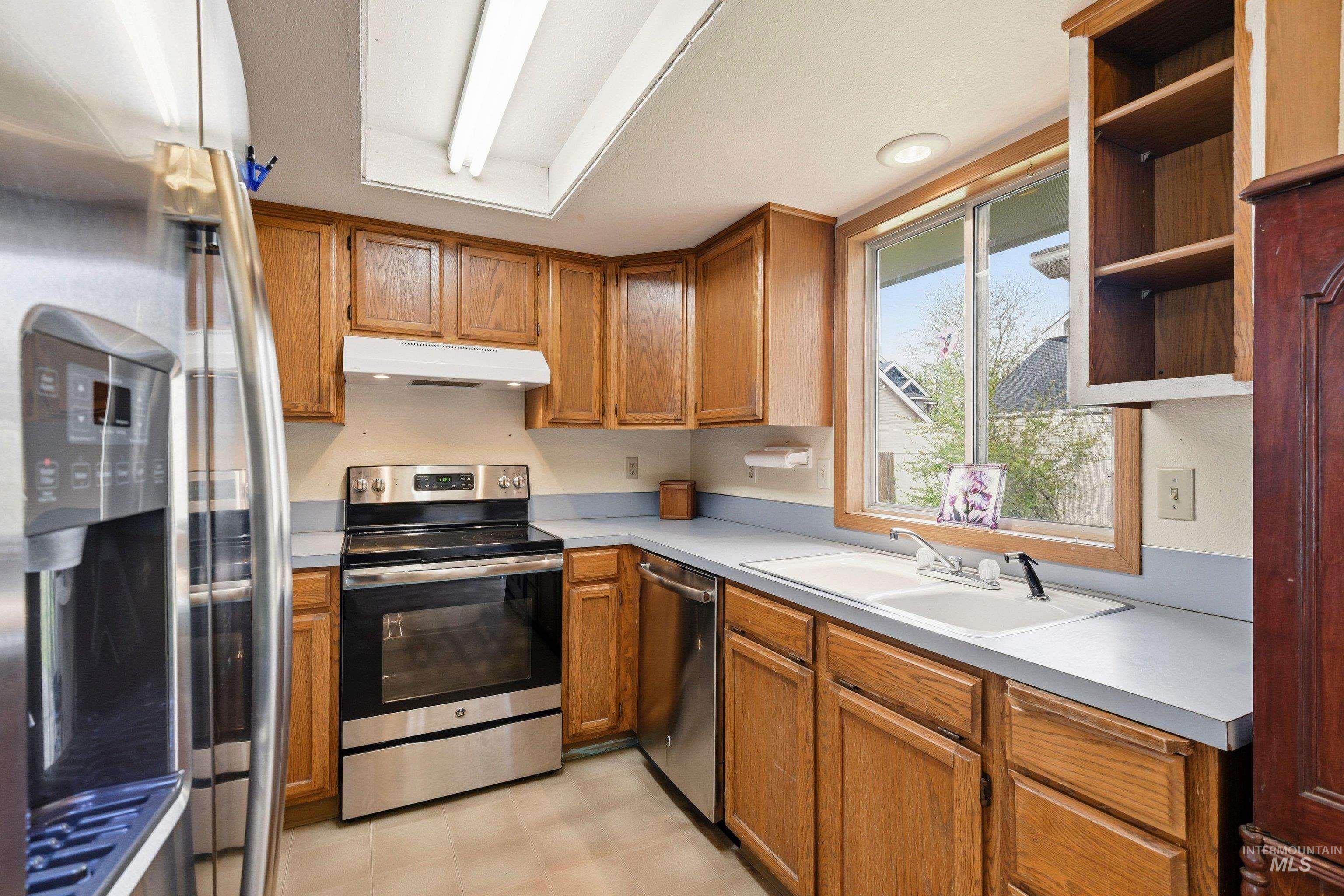 Kitchen featuring stainless steel appliances, light countertops, wood finish cabinets, light floors, and open shelves