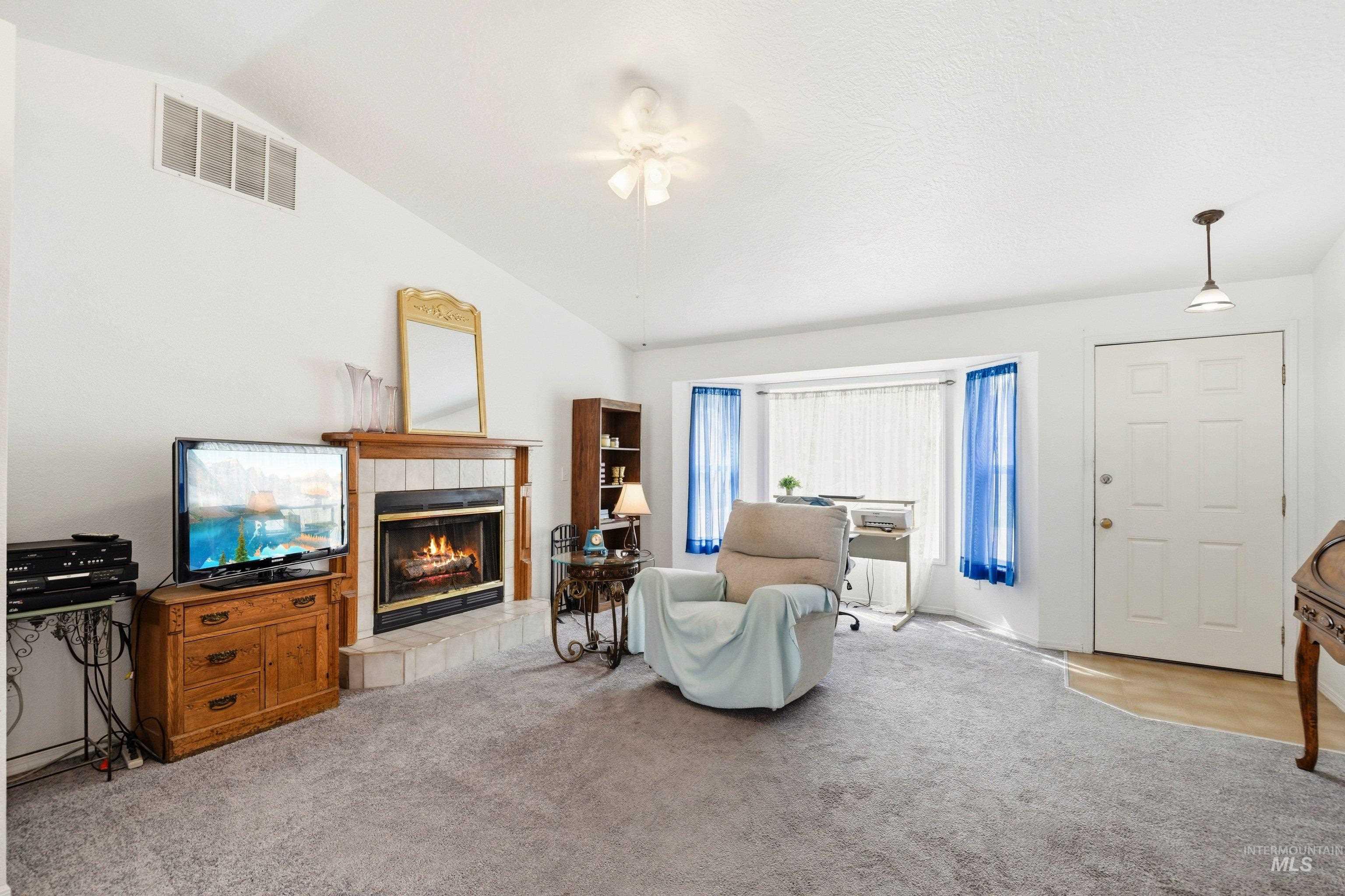 Living room with a tile fireplace, light colored carpet, lofted ceiling, and a ceiling fan