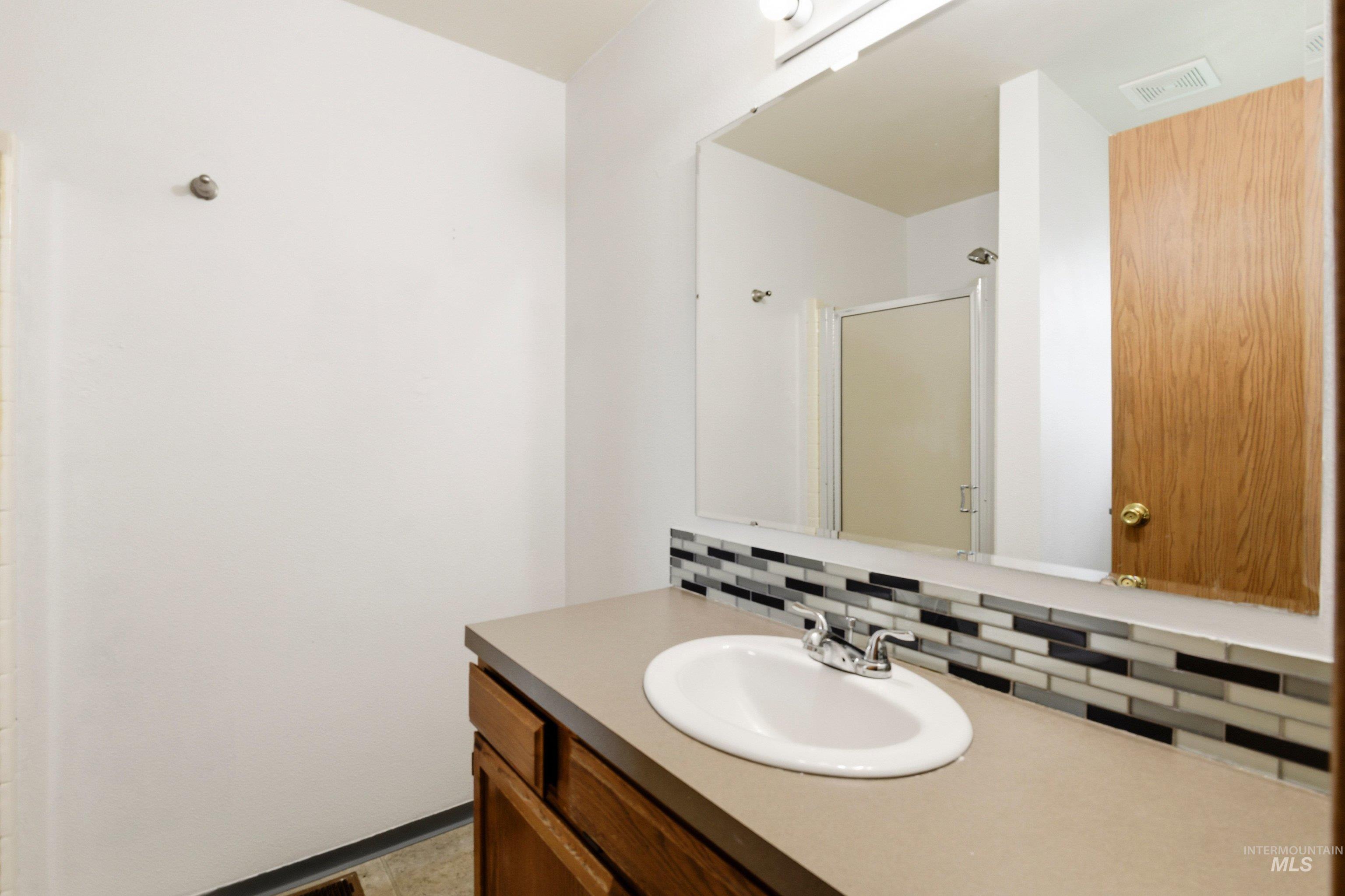 Full bathroom with a shower stall, vanity, and decorative backsplash