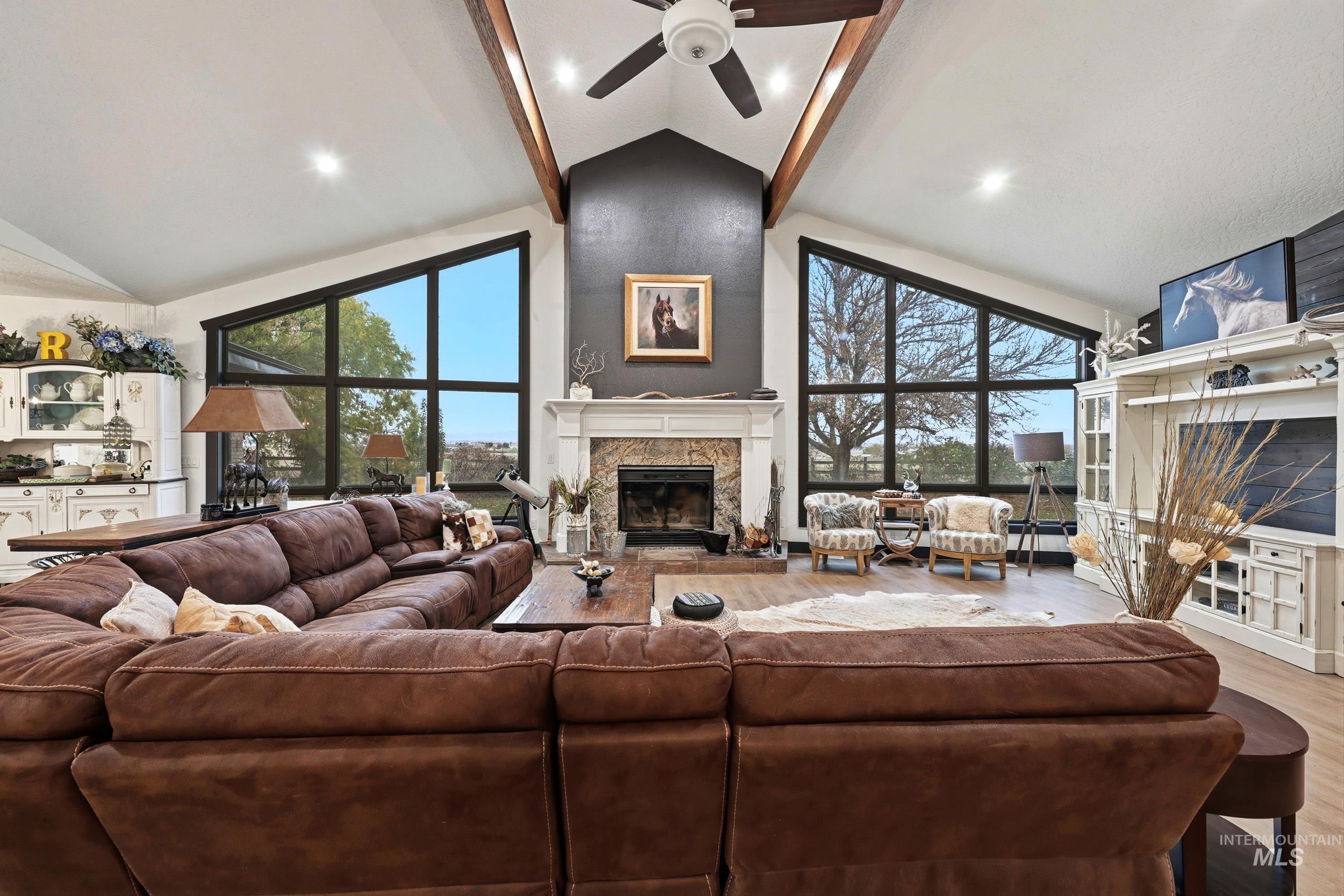 Living area featuring a fireplace, light wood-type flooring, high vaulted ceiling, ceiling fan, and beamed ceiling