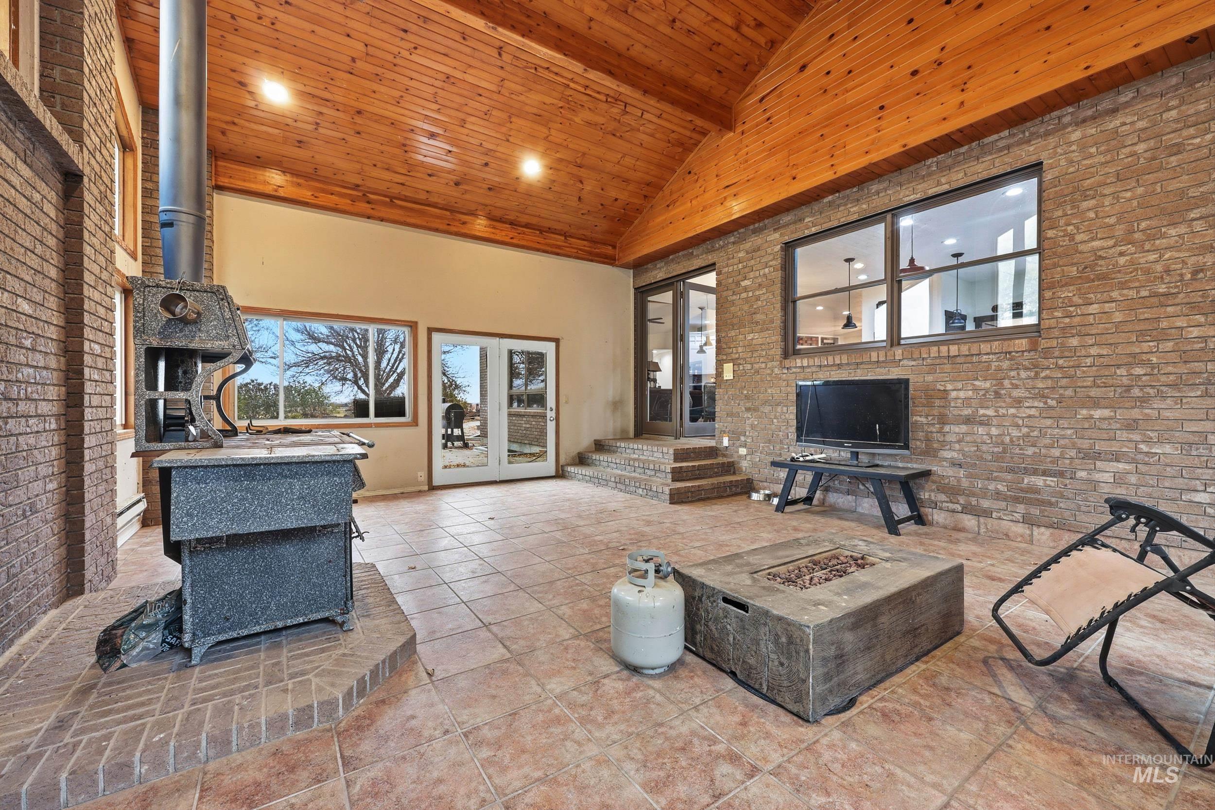 Living room featuring brick wall, a wood stove, high vaulted ceiling, tile patterned flooring, and wood ceiling