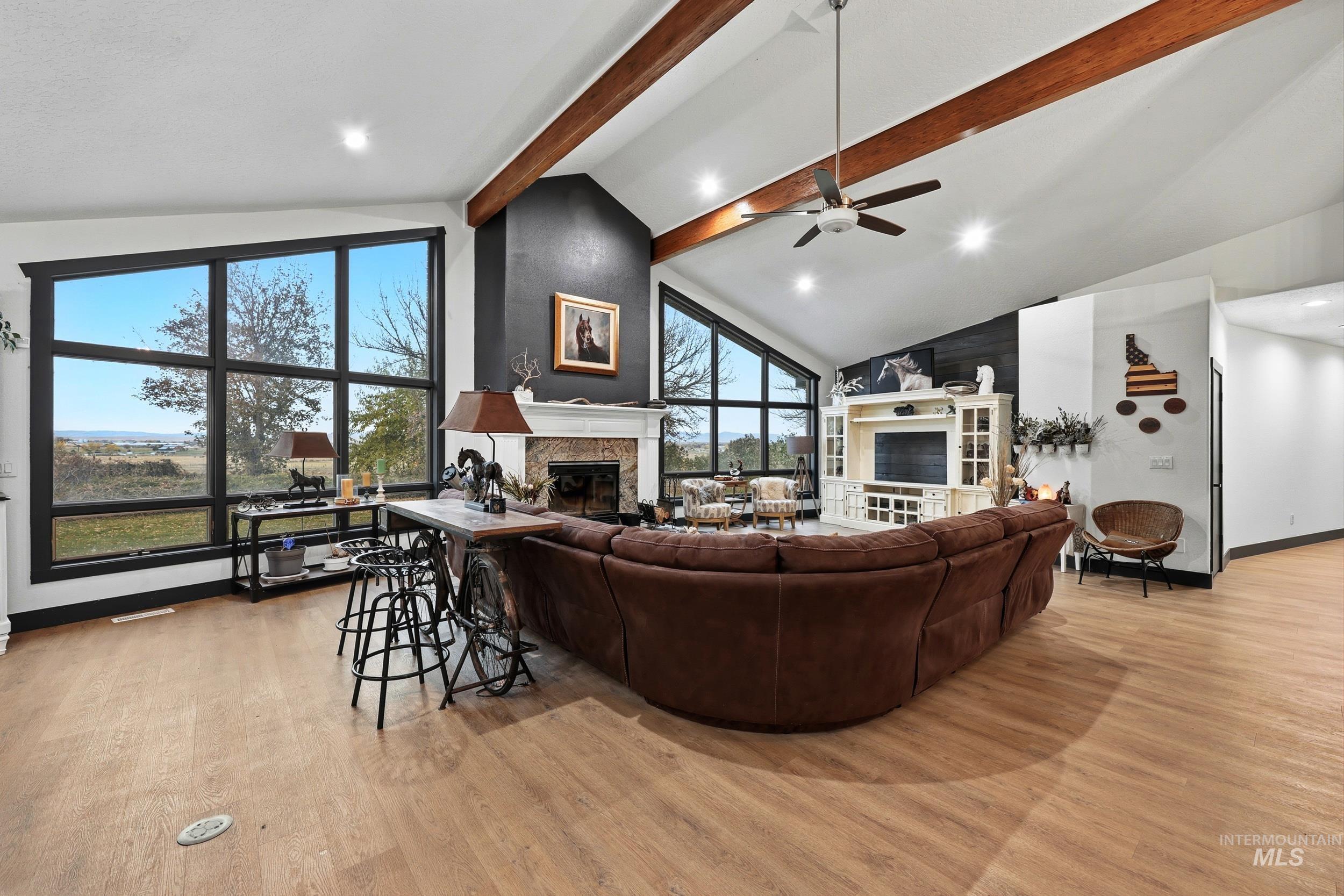 Living area with light wood-type flooring, beam ceiling, a glass covered fireplace, recessed lighting, and ceiling fan