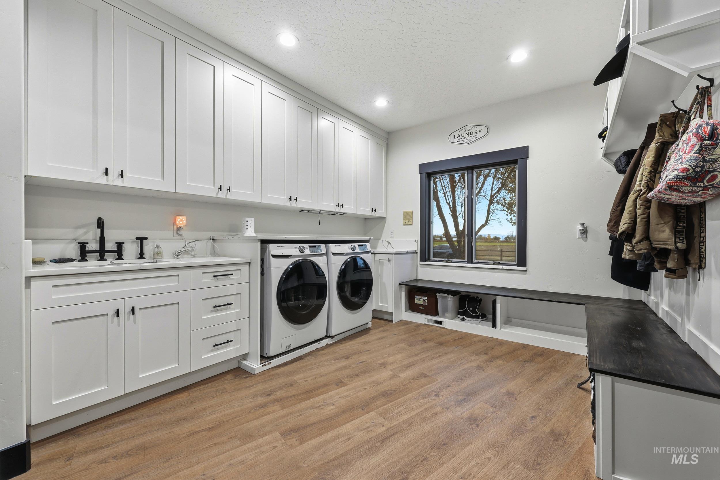 Washroom with cabinet space, light wood finished floors, washer and dryer, recessed lighting, and a textured ceiling