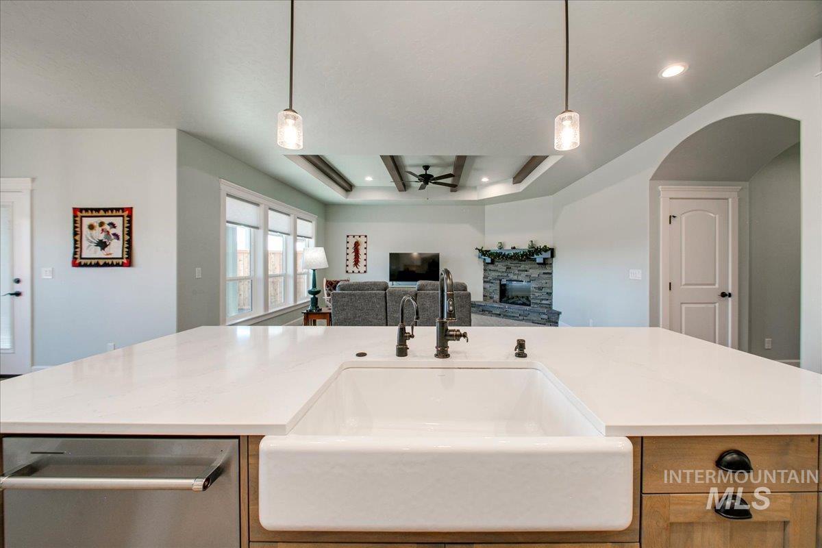 Kitchen featuring a fireplace, stainless steel dishwasher, pendant lighting, and a raised ceiling