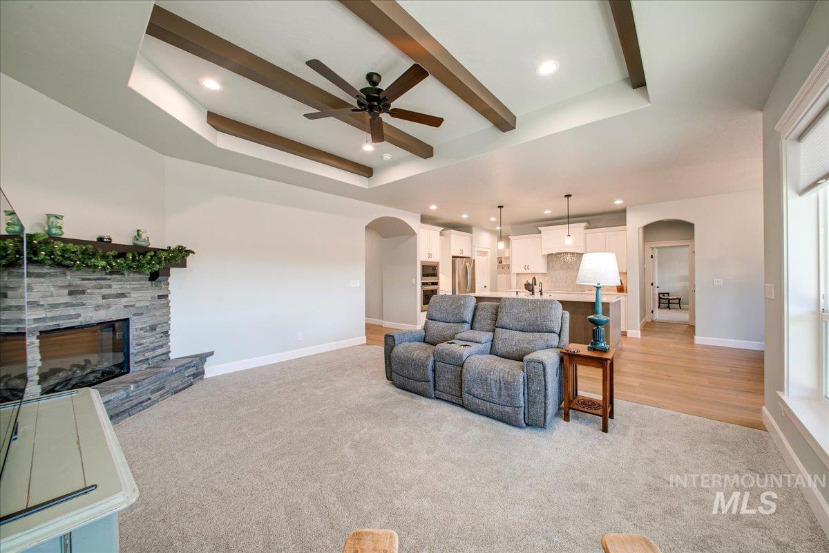 Living area featuring arched walkways, a stone fireplace, light colored carpet, beam ceiling, and recessed lighting