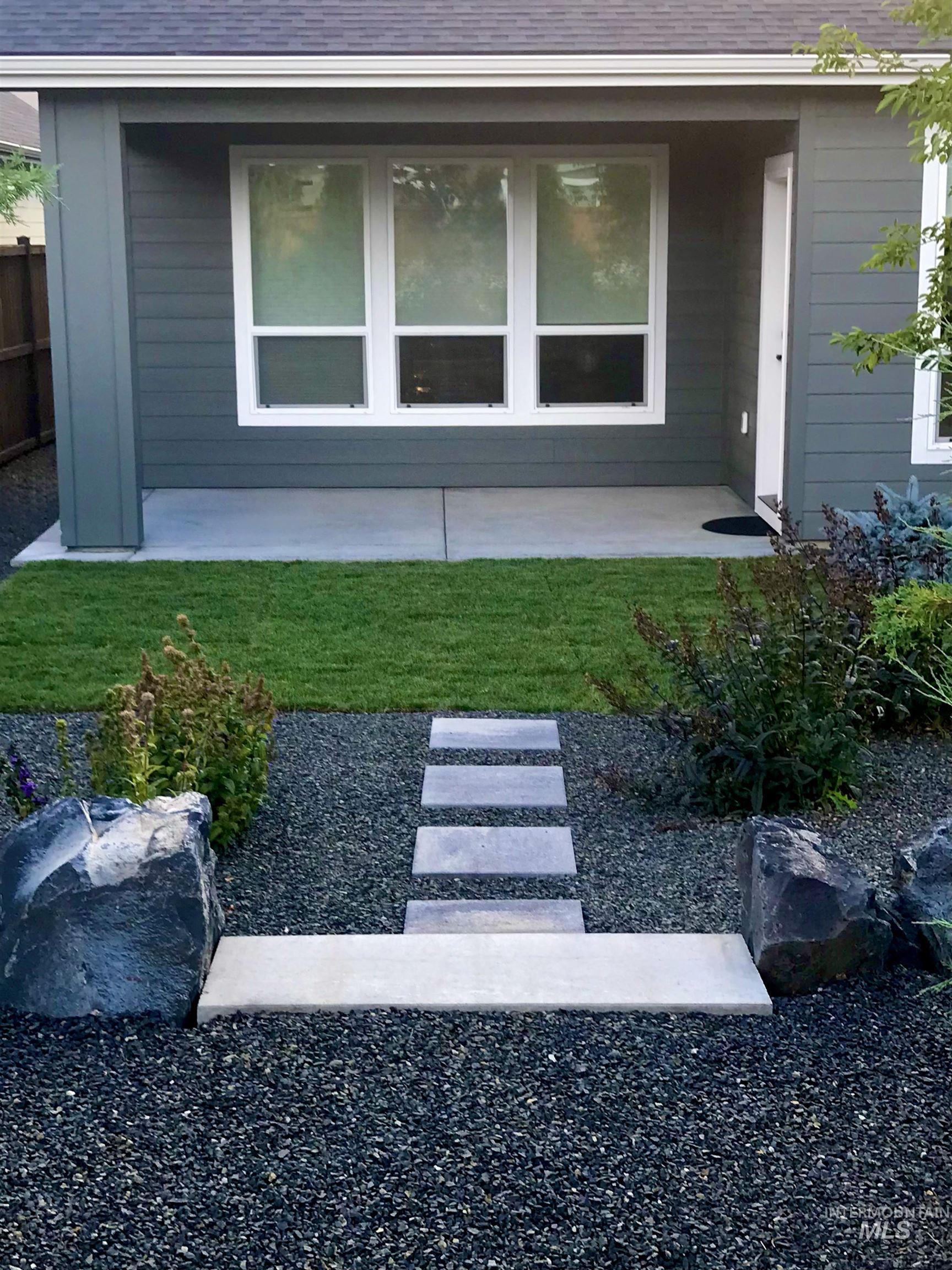 Rear exterior featuring modern gray siding, white-framed windows, 12'x14' grass area, and a concrete patio.