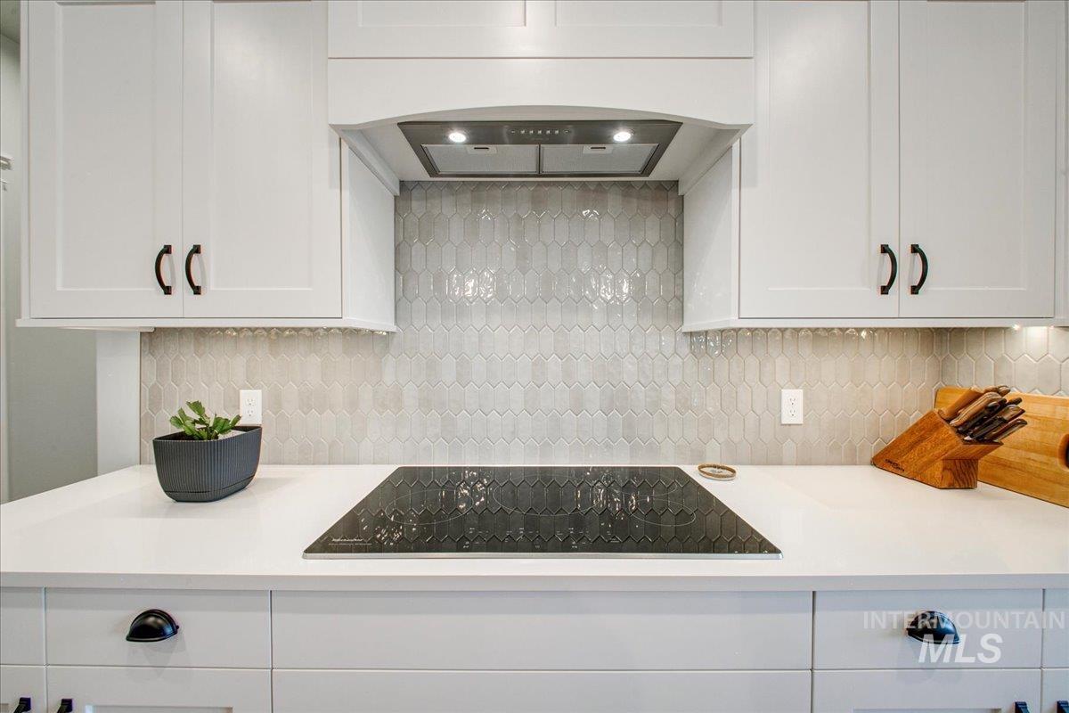 Kitchen featuring white cabinetry, custom range hood, black electric cooktop, and backsplash
