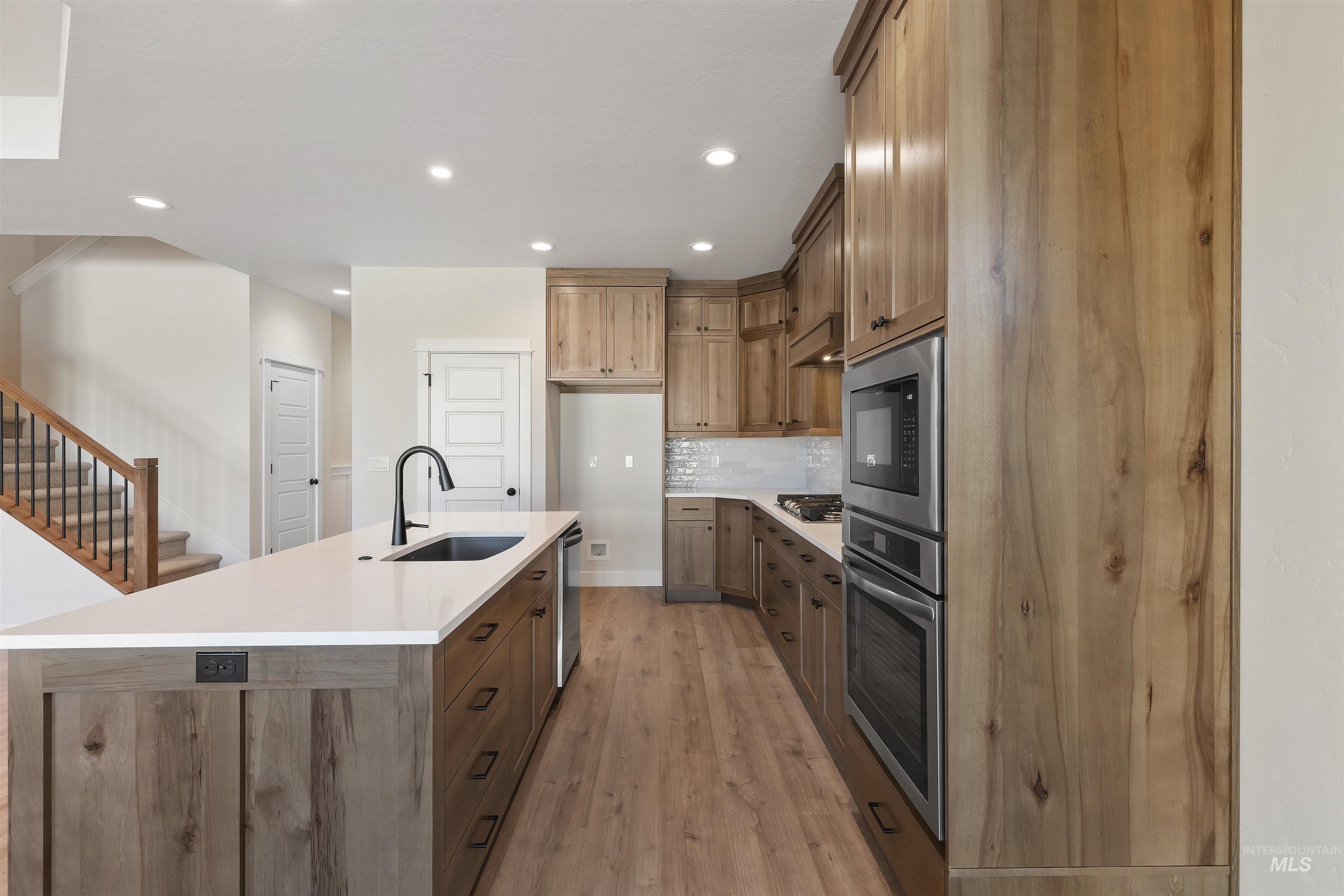 Kitchen featuring stainless steel appliances, wood finish cabinets, a kitchen island with sink, light wood finished floors, and decorative backsplash