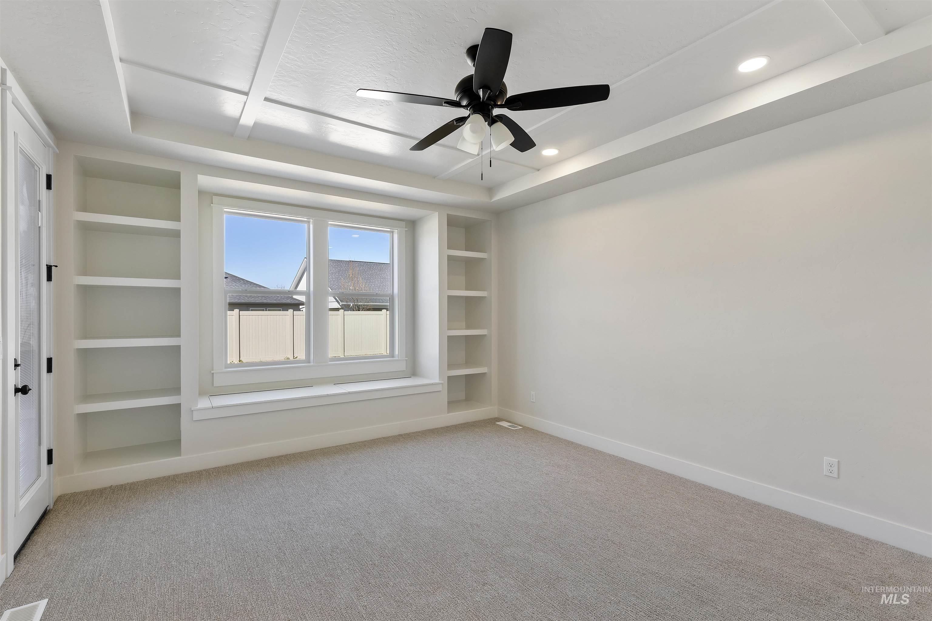 Spare room with built in shelves, ceiling fan, light colored carpet, and a tray ceiling