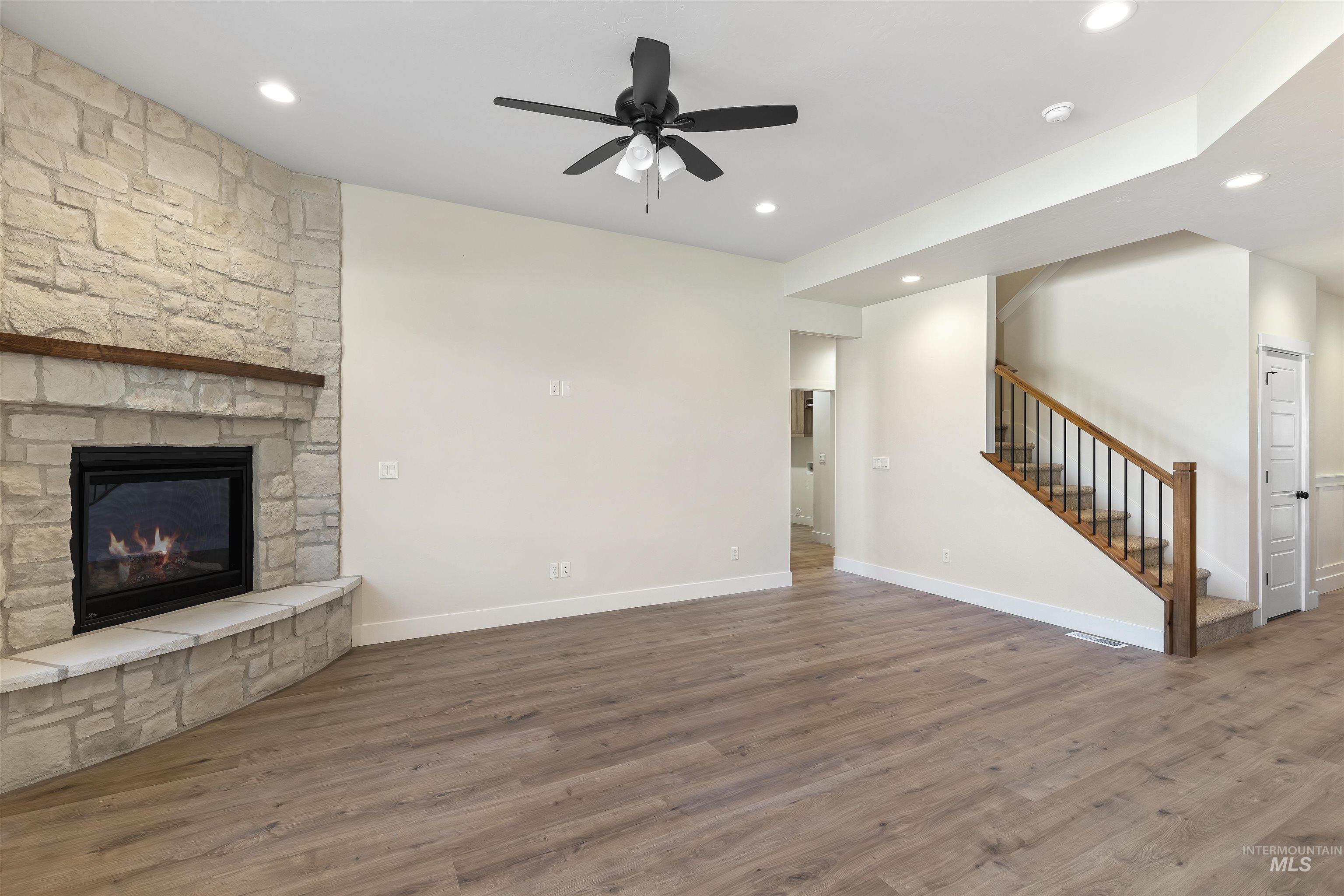 Unfurnished living room featuring a ceiling fan, dark wood-style flooring, a stone fireplace, and recessed lighting