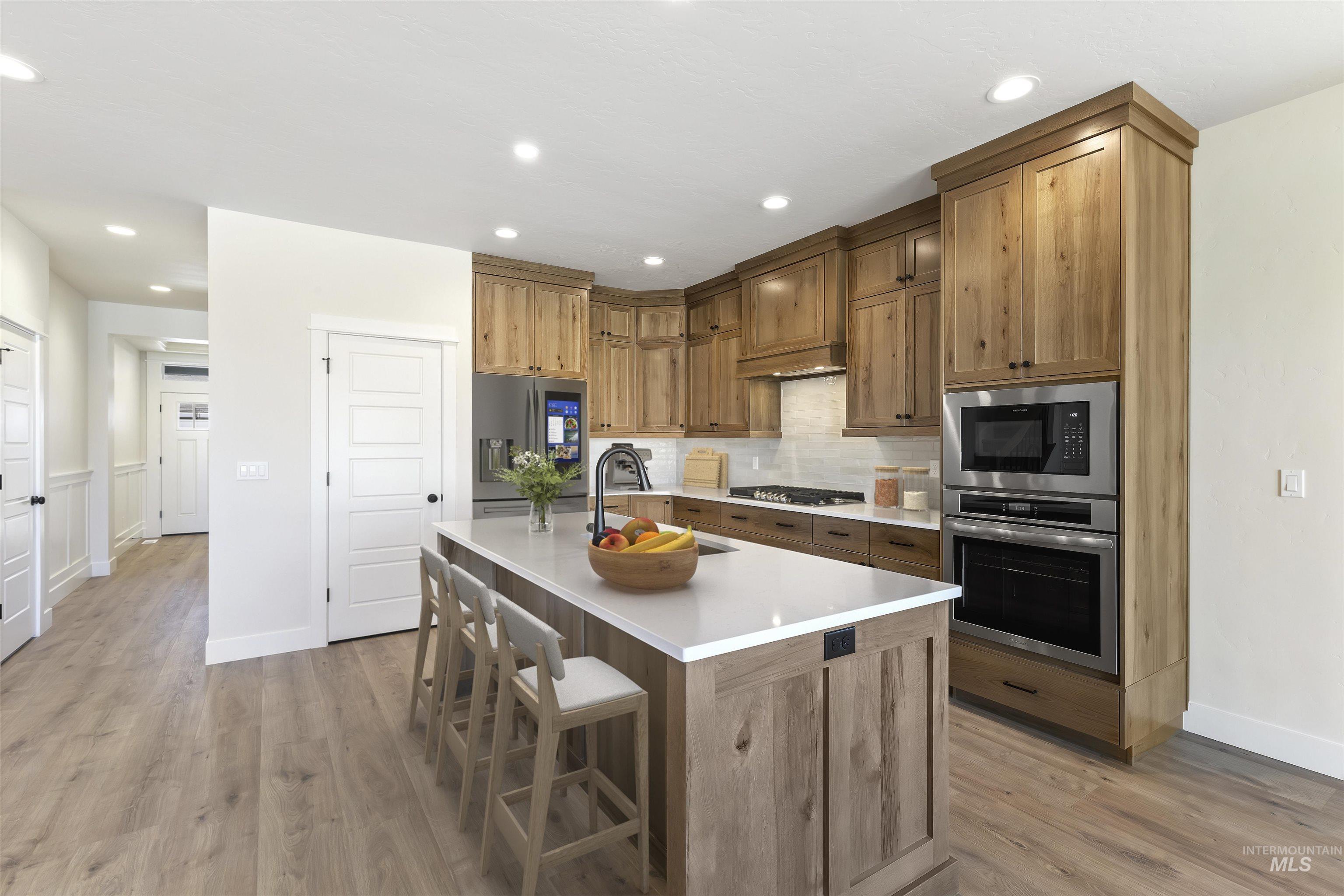 Kitchen featuring stainless steel appliances, light wood-type flooring, a center island with sink, a kitchen bar, and backsplash