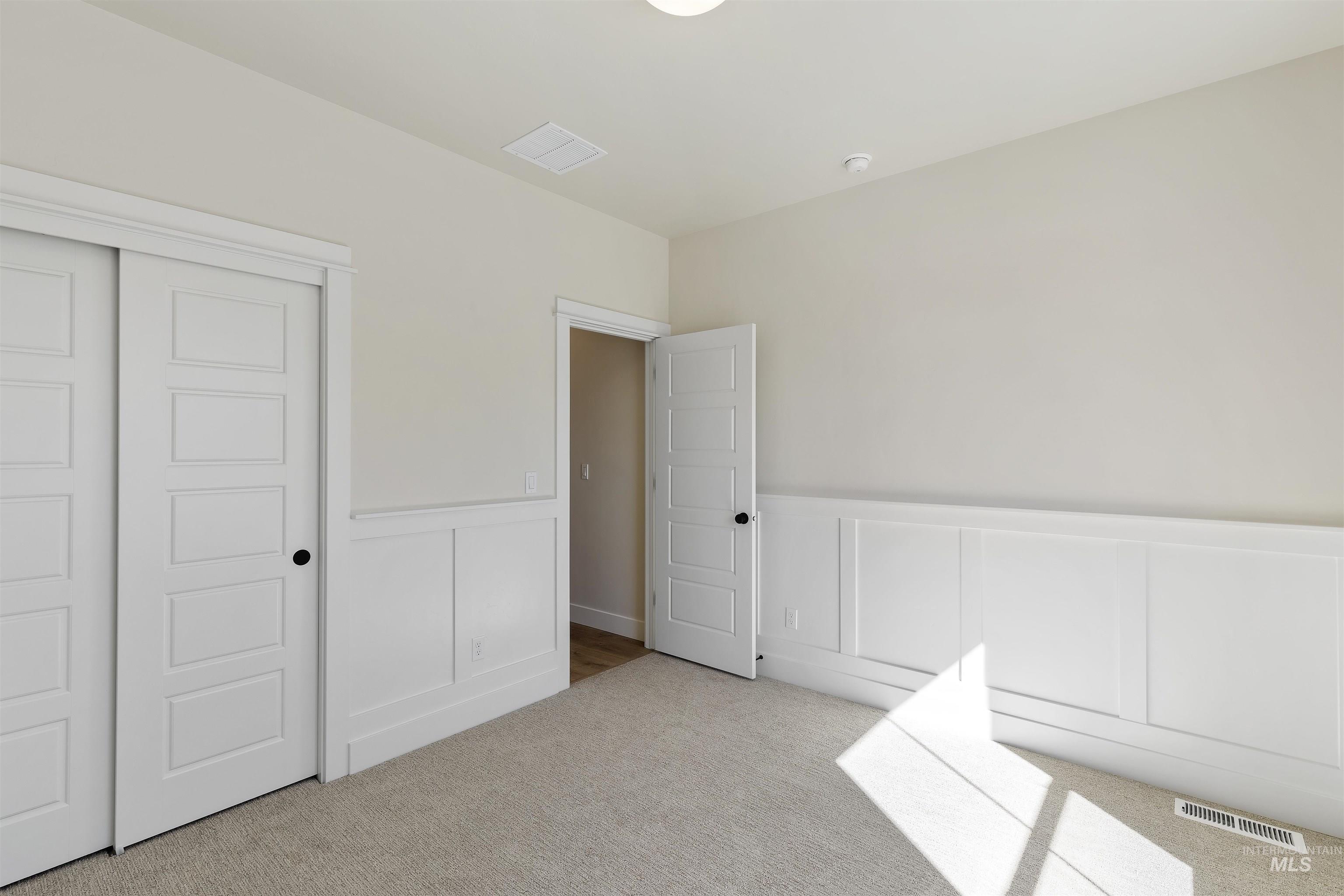 Unfurnished bedroom featuring a decorative wall, a wainscoted wall, light carpet, and a closet