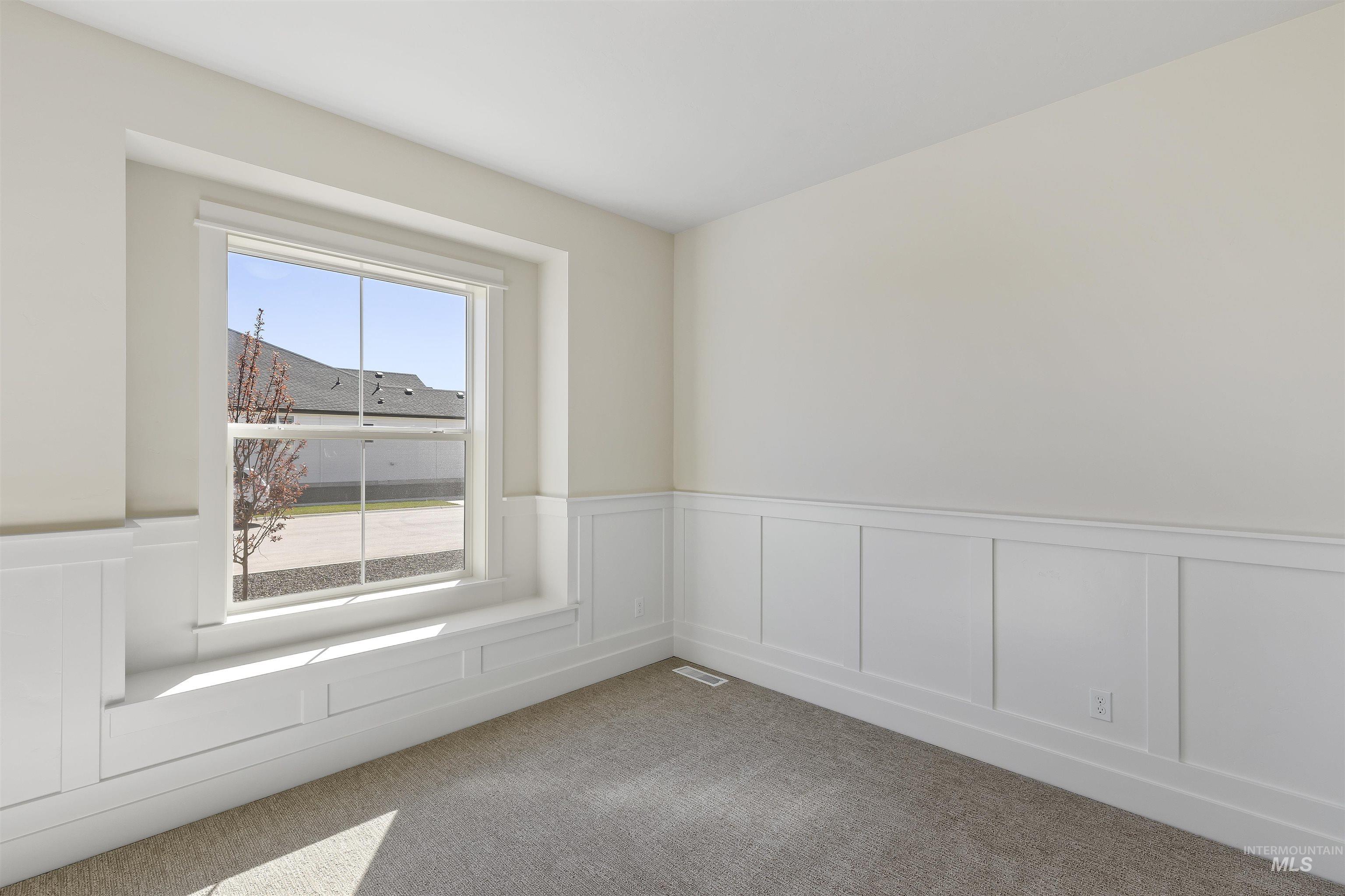 Spare room featuring wainscoting, a decorative wall, and light carpet