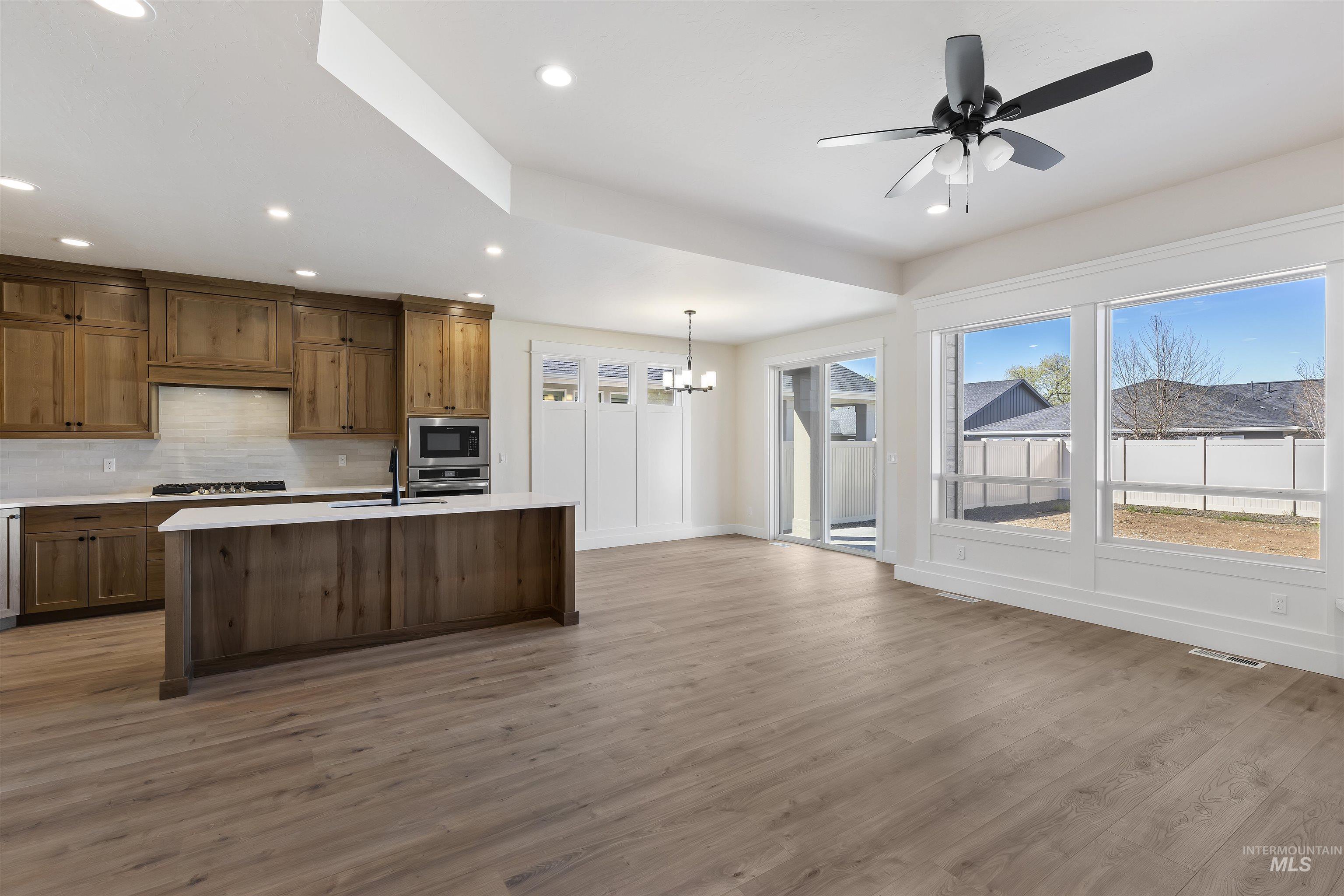 Kitchen featuring ceiling fan, decorative backsplash, light wood finished floors, a center island with sink, and a chandelier