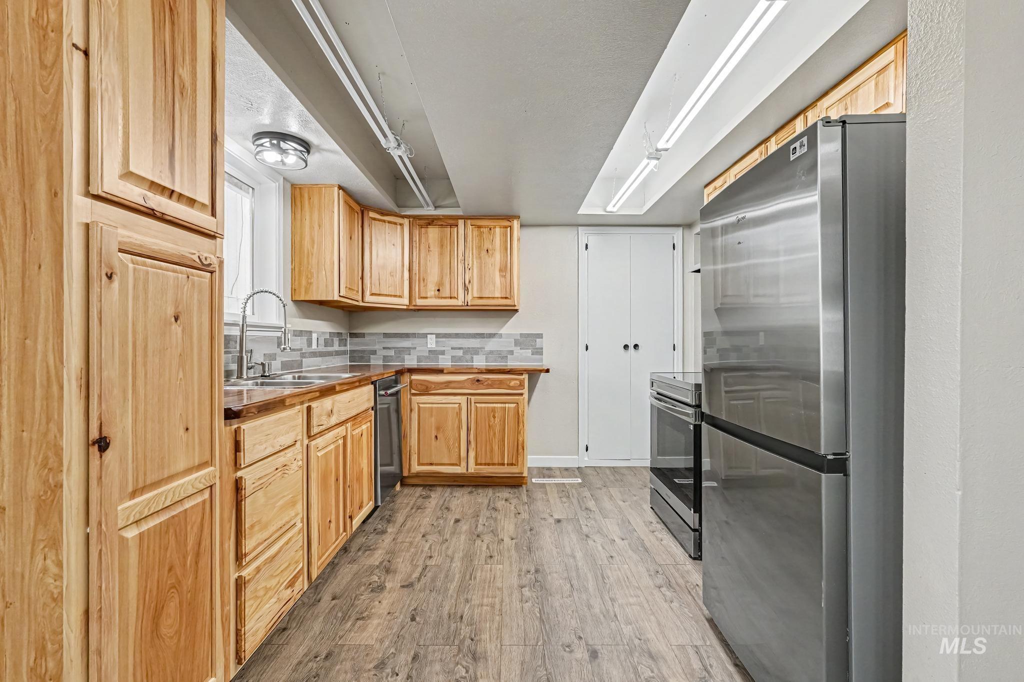 Kitchen featuring extensive natural wood cabinetry, wood-finish flooring, stainless steel appliances, a tile backsplash, and recessed lighting