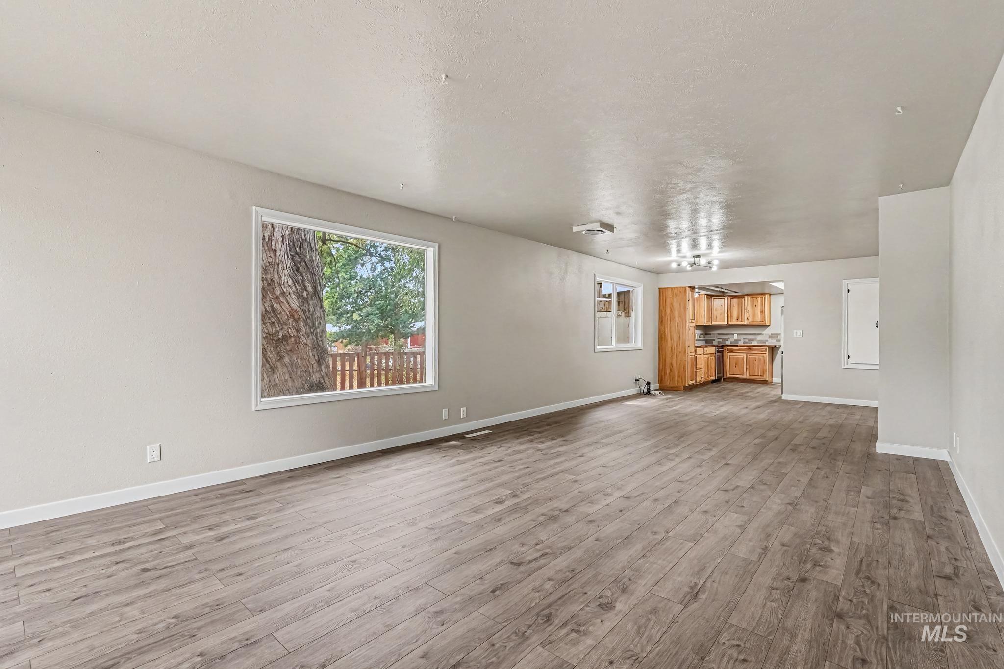 Spacious open-concept room featuring wood-finish flooring, neutral wall tones, and a large window