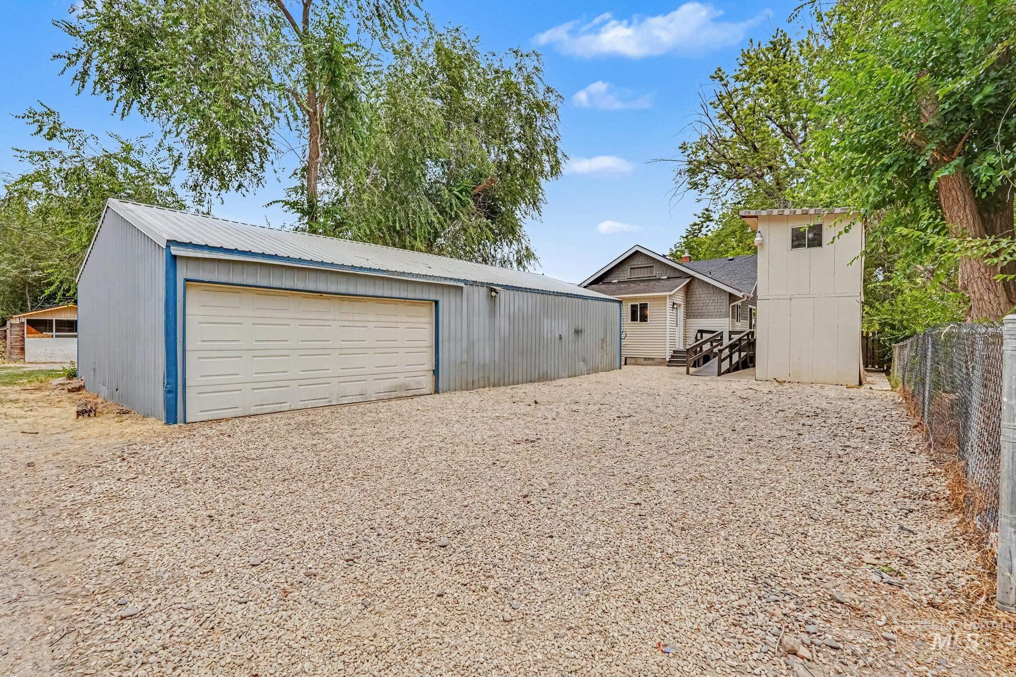 Spacious gravel lot featuring a large metal-sided outbuilding with a roll-up garage door, a separate two-story structure, and a fenced perimeter